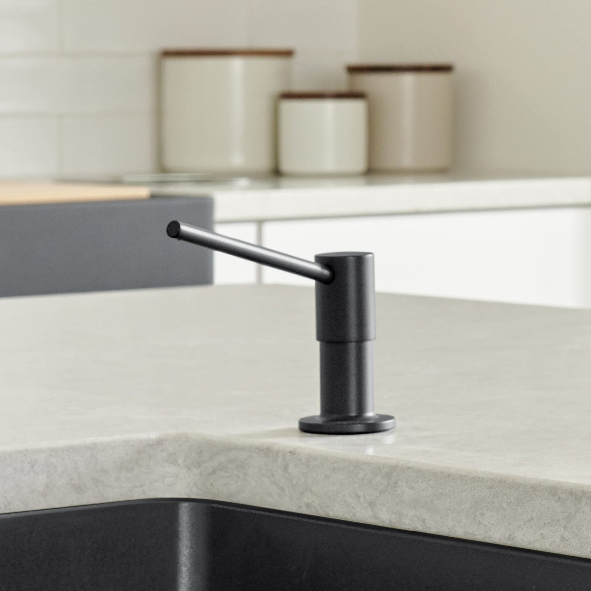 Coal black soap dispenser with angled pump spout mounted on light stone countertop.