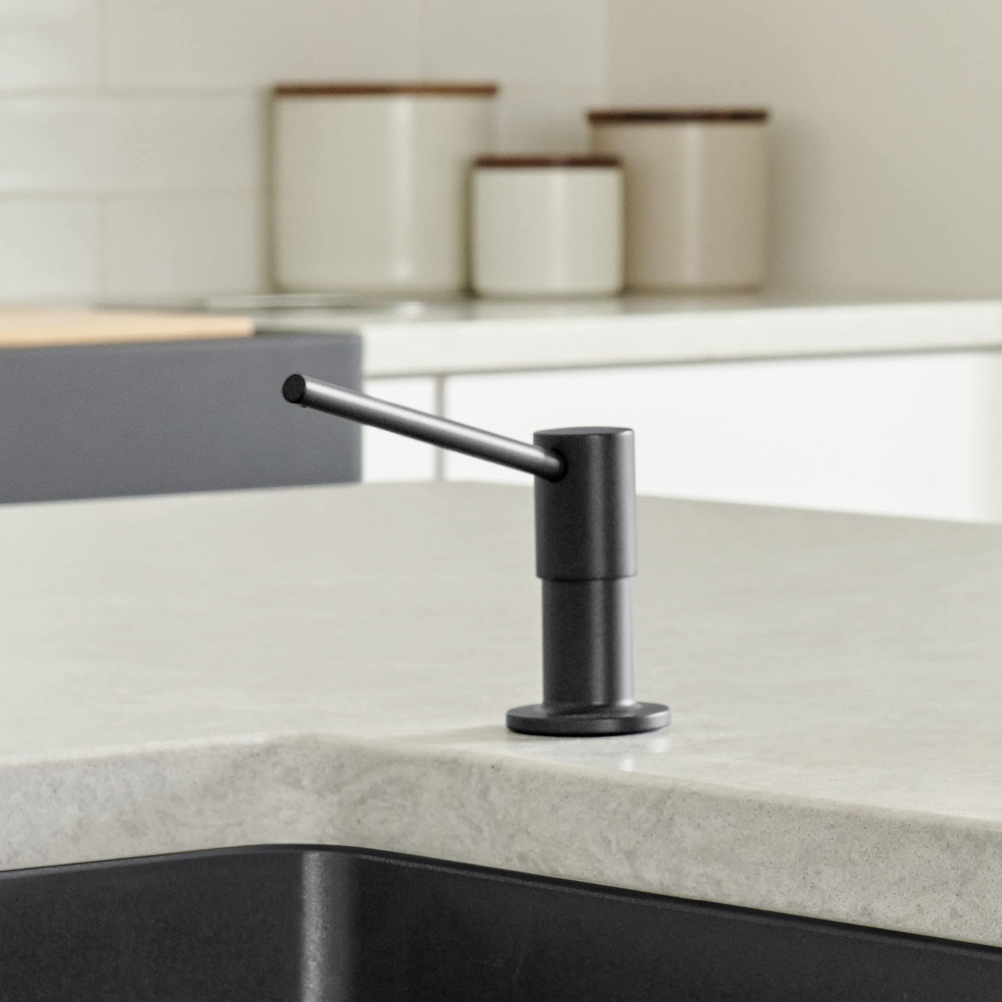 Coal black soap dispenser with angled pump spout mounted on light stone countertop.