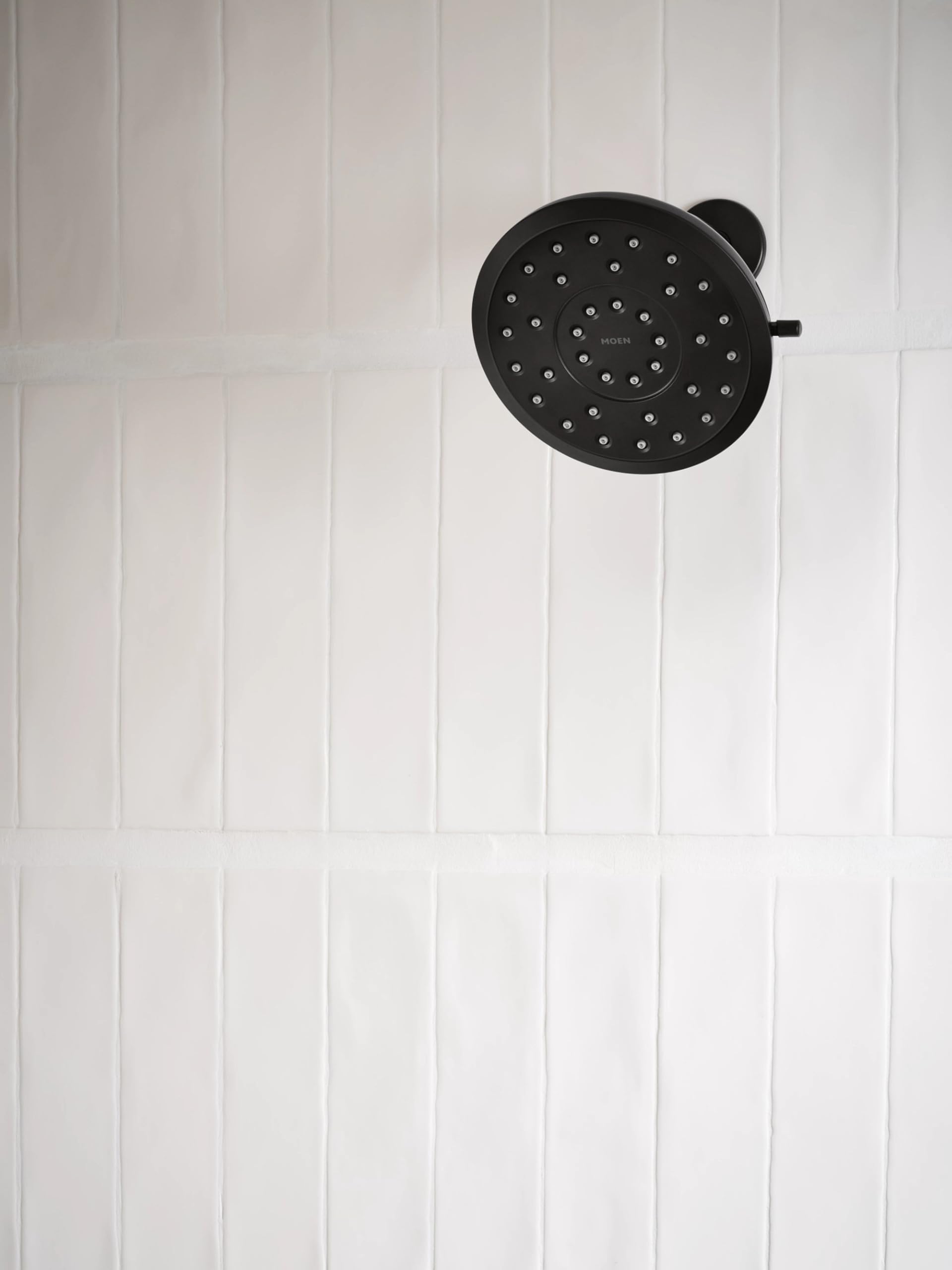 Matte black round shower head with multiple spray jets mounted on white tile wall.