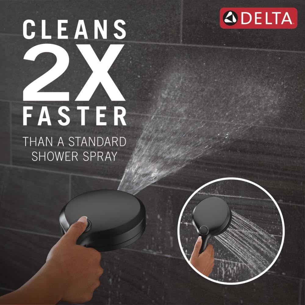 Matte black circular shower head held in hand, spraying water against dark tile background.
