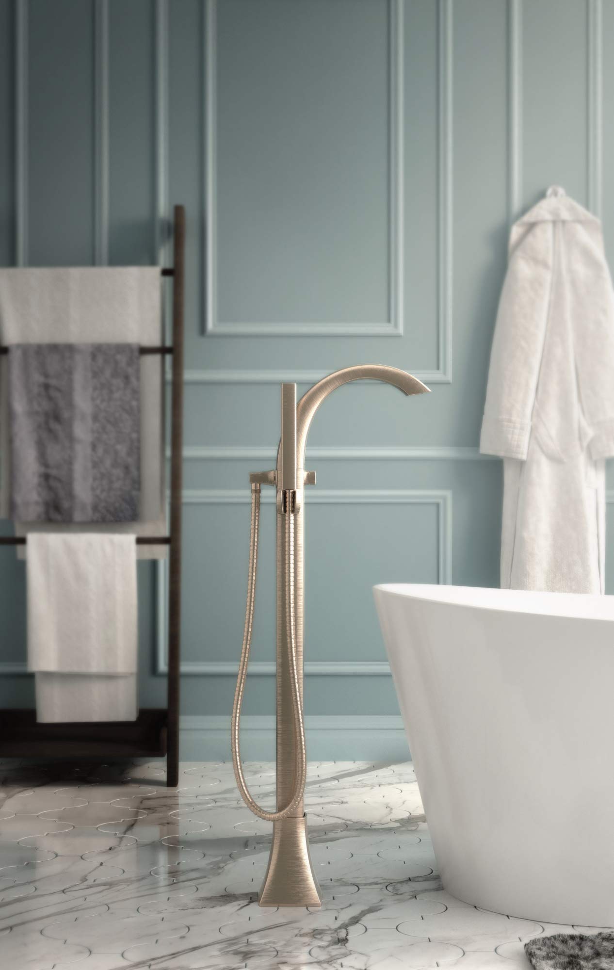 Champagne bronze floor-mount tub filler with curved spout and hand shower hose, installed next to freestanding white bathtub.