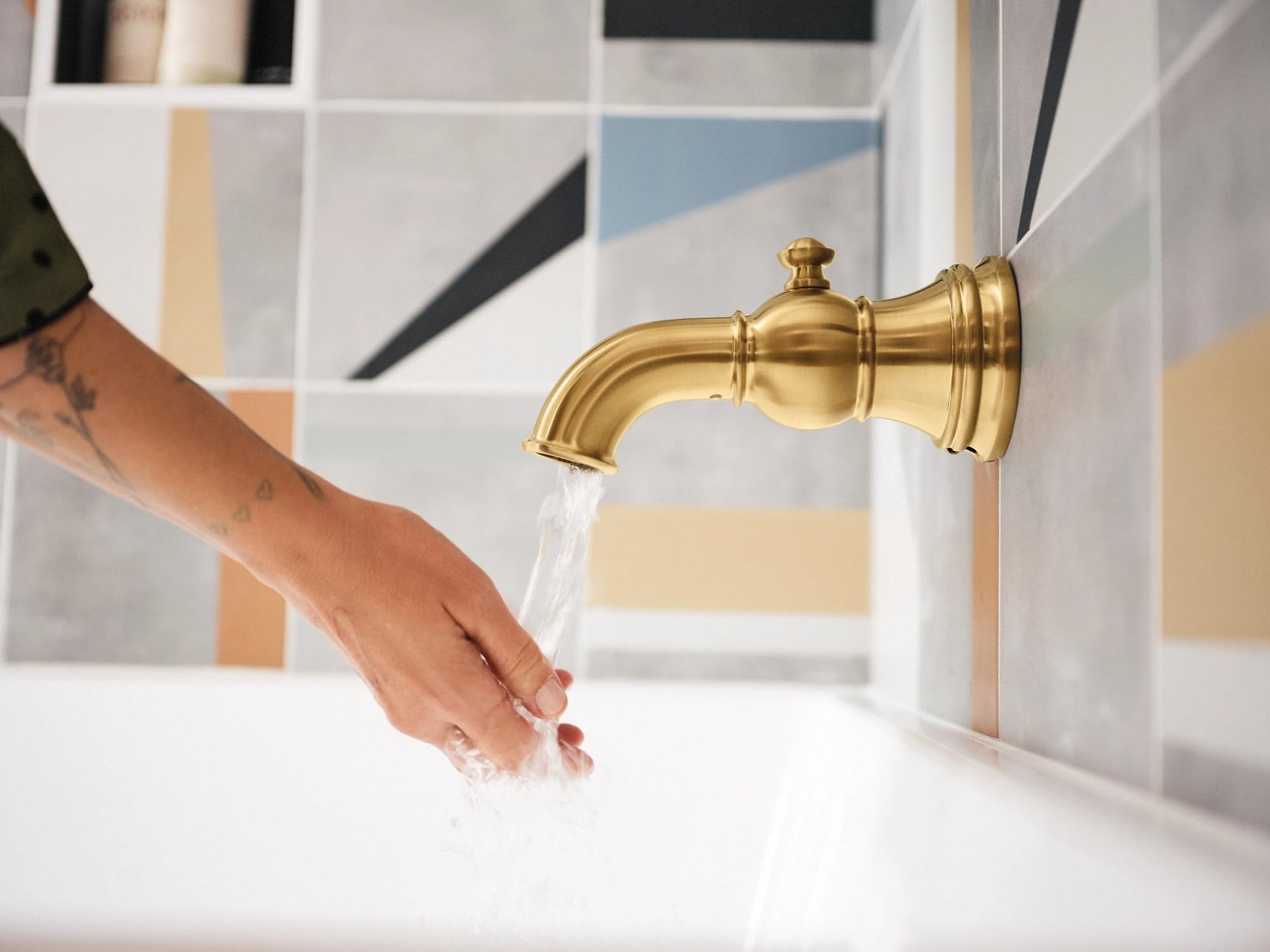 Brushed gold tub spout with water running over a hand in a bathroom sink.