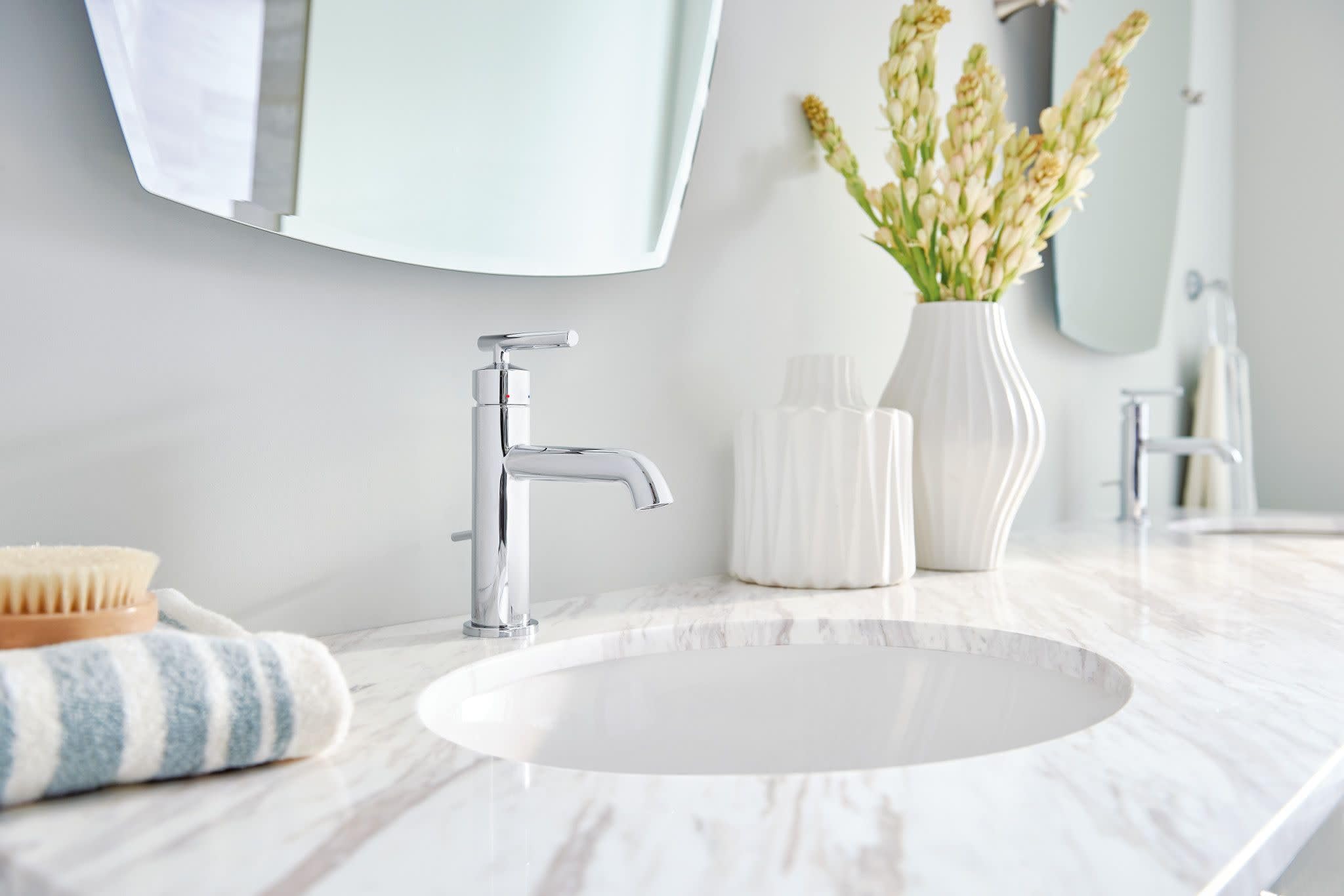 Chrome single-handle bathroom faucet mounted on marble countertop with round white sink basin.