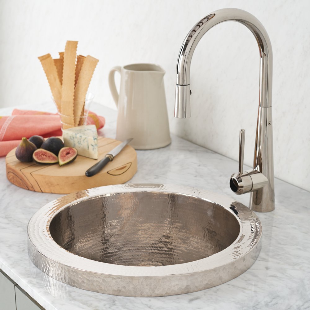 Polished nickel circular prep sink with hammered interior and matching pull-down faucet on marble countertop.