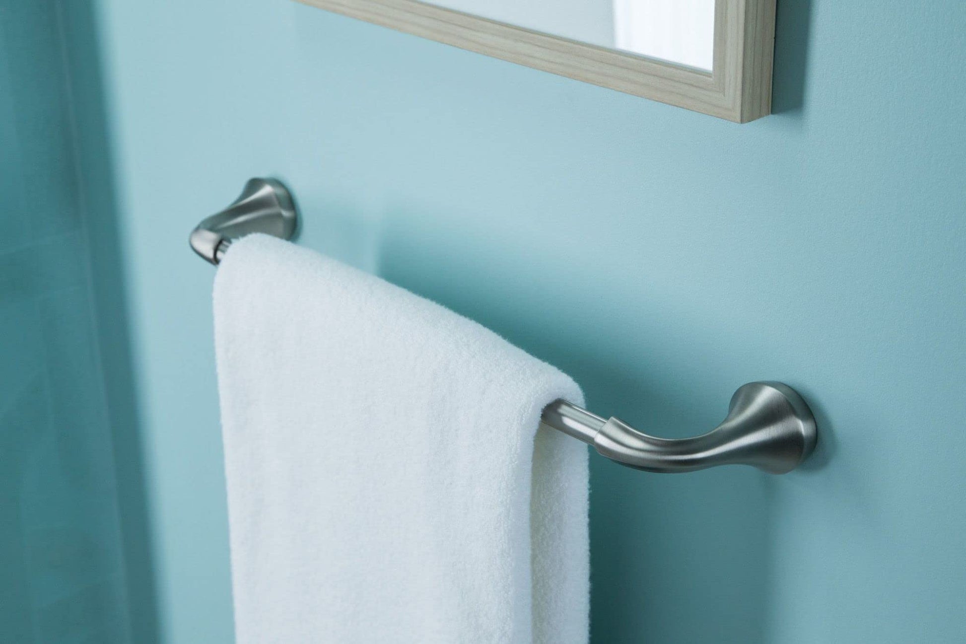 Brushed nickel curved towel bar mounted on light blue wall with white towel draped over it.