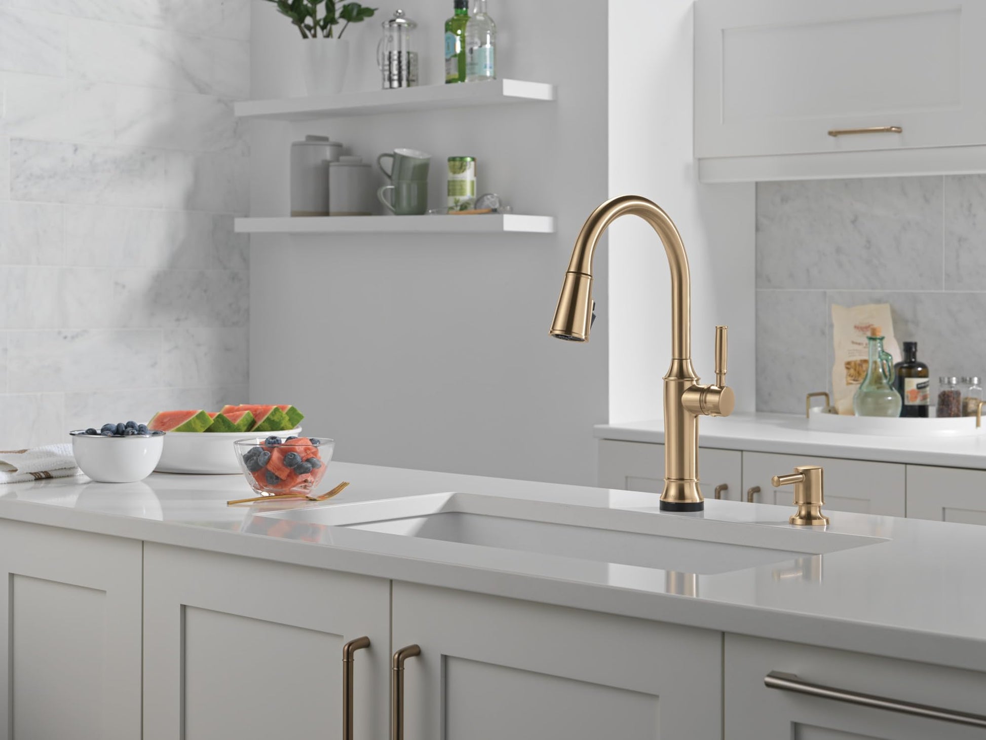 Champagne bronze metal soap dispenser with cylindrical pump, positioned next to kitchen faucet on white countertop.