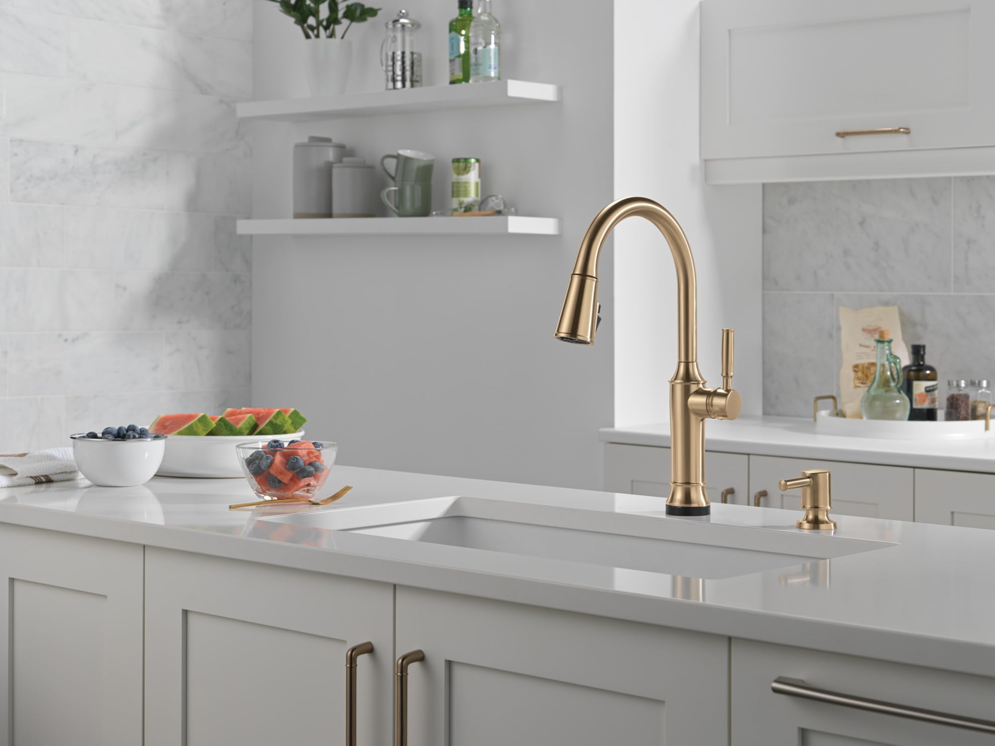 Champagne bronze metal soap dispenser with cylindrical pump, positioned next to kitchen faucet on white countertop.