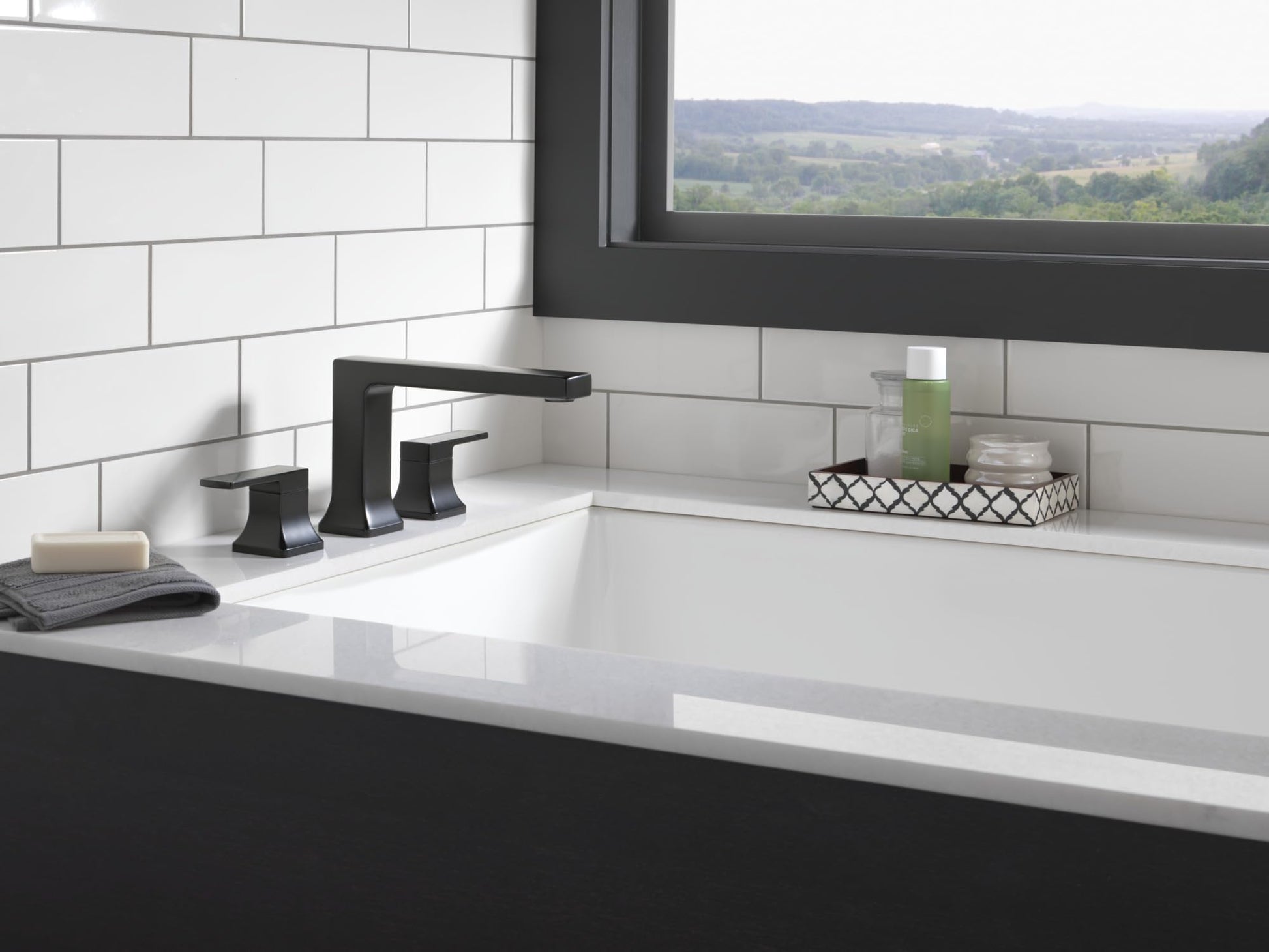 Matte black Delta Velum roman tub trim with two handles and spout installed on white bathroom countertop.