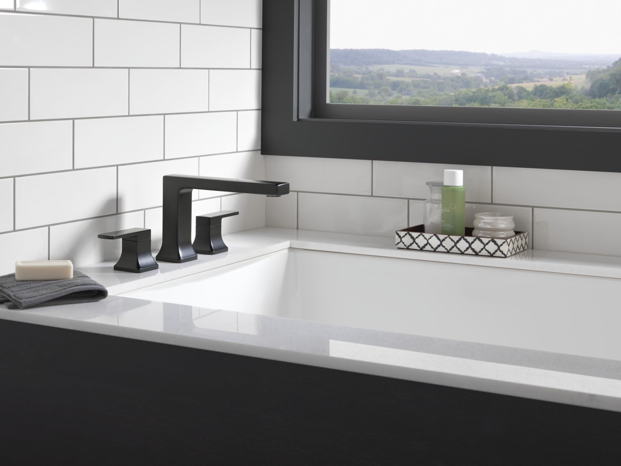 Matte black Delta Velum roman tub trim with two handles and spout installed on white bathroom countertop.