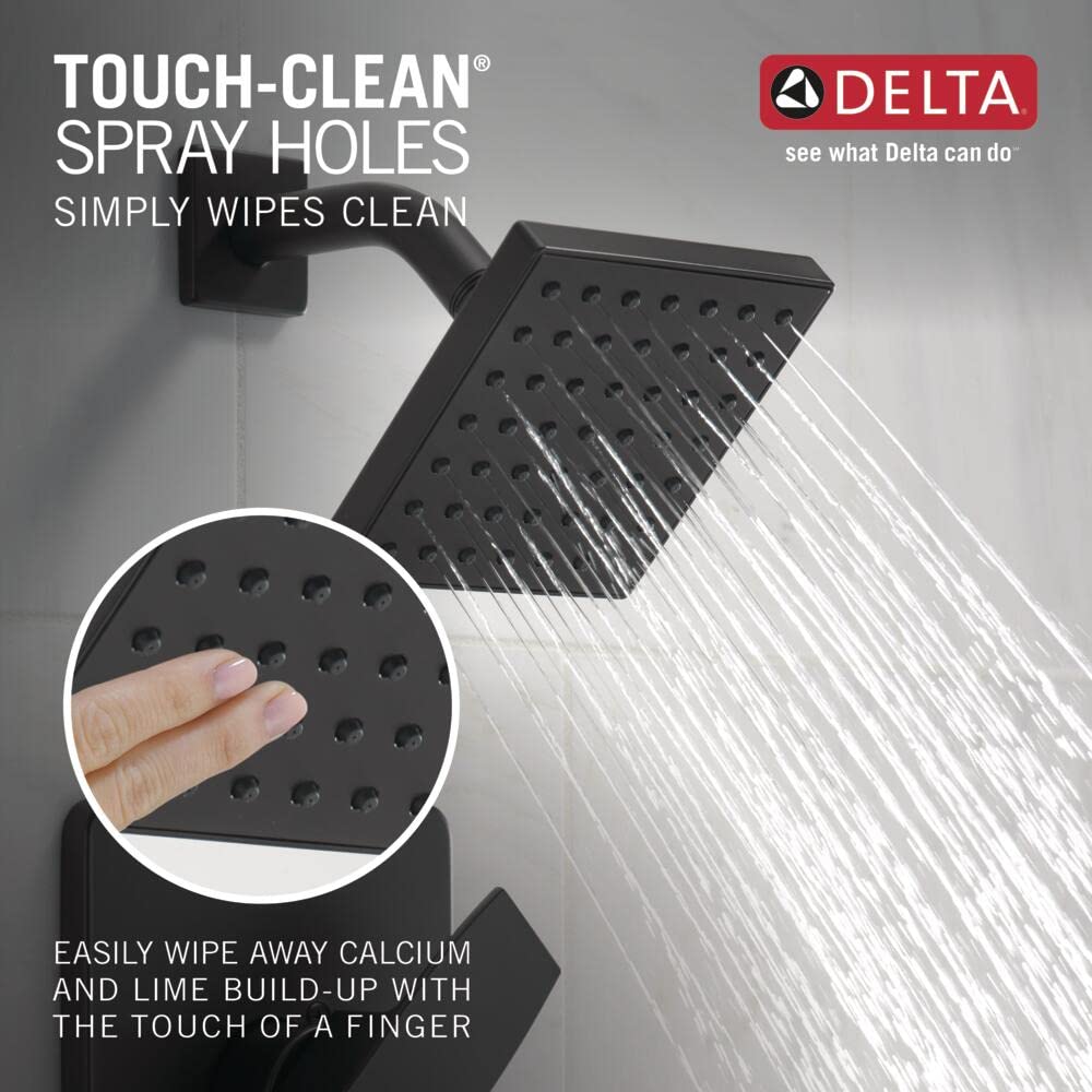 Matte black square shower head mounted on wall with water spraying downward, showing spray holes design.