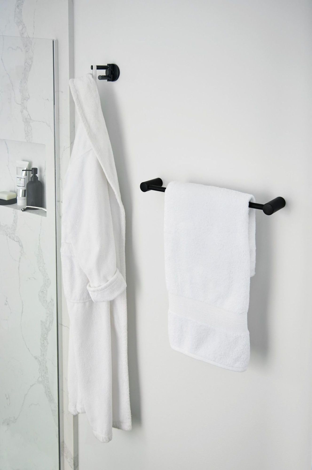 Matte black double swivel robe hook mounted on white bathroom wall with white towels and robe hanging.