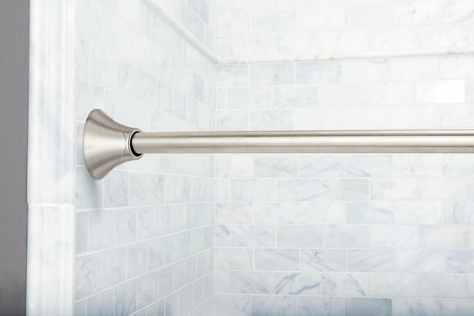 Curved brushed nickel shower rod with cone-shaped end cap mounted on white subway tile wall.