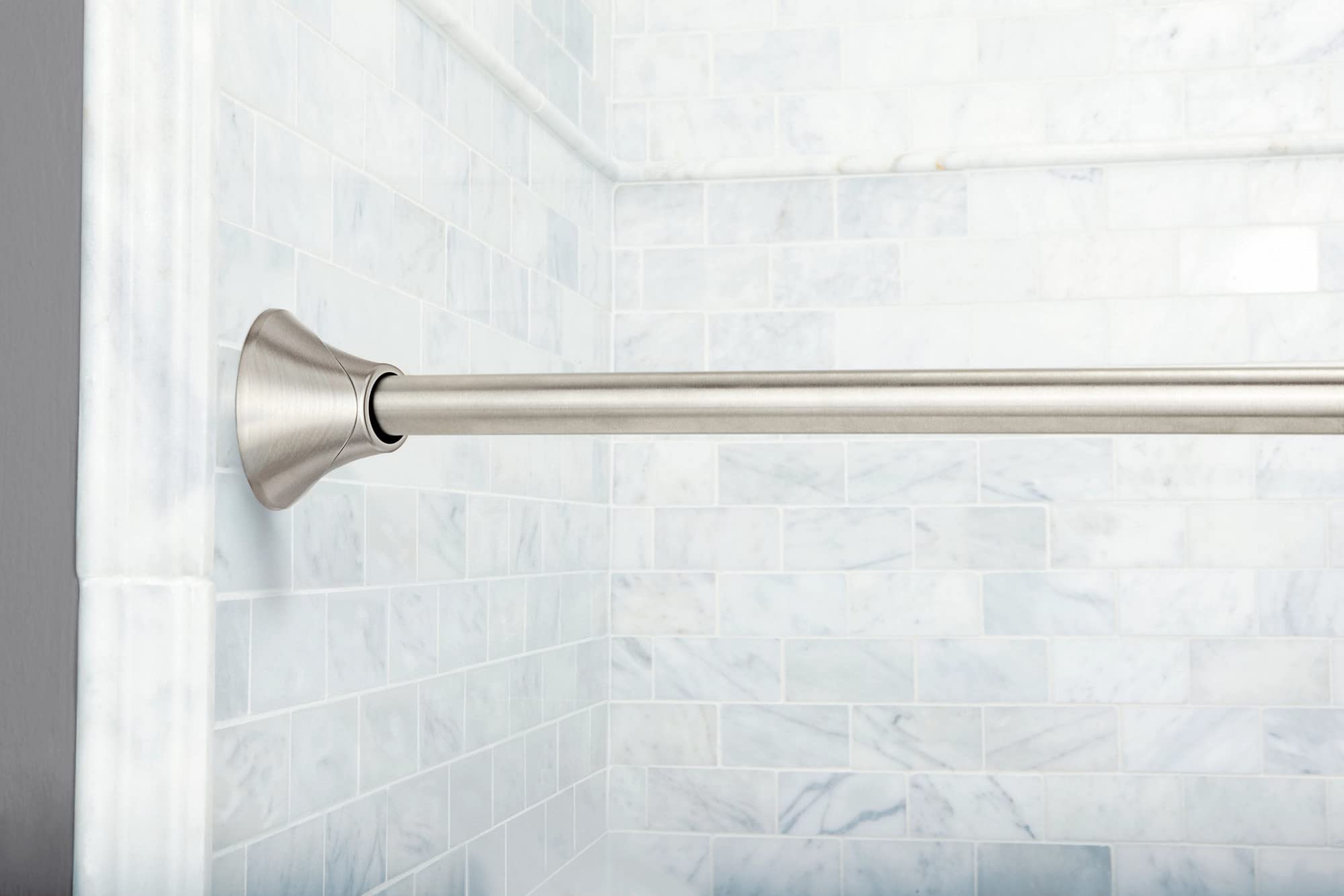 Curved brushed nickel shower rod with cone-shaped end cap mounted on white subway tile wall.
