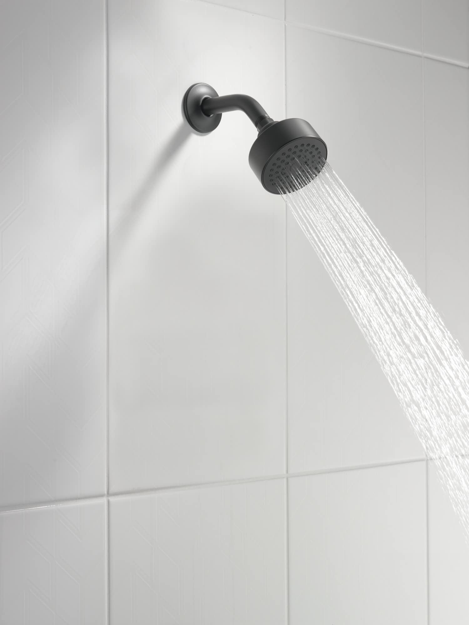 Matte black curved shower arm with round shower head mounted on white tile wall, water streaming downward.