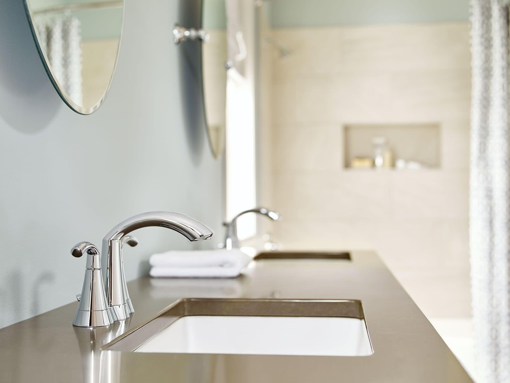 Chrome bathroom faucet with high arc spout and two lever handles mounted on vanity sink.