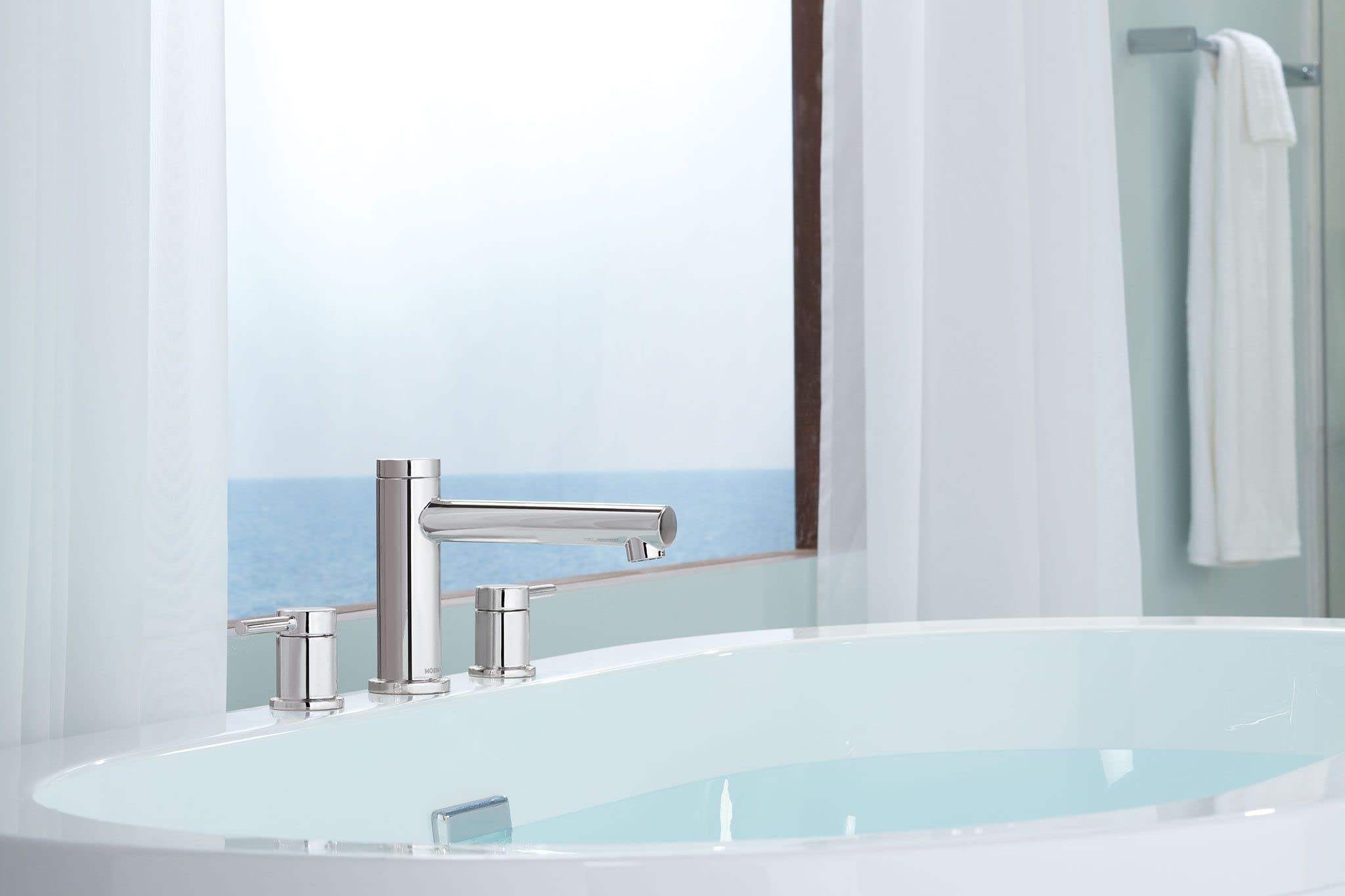 Chrome two-handle Roman tub faucet with deck mount spout installed on white bathtub edge.