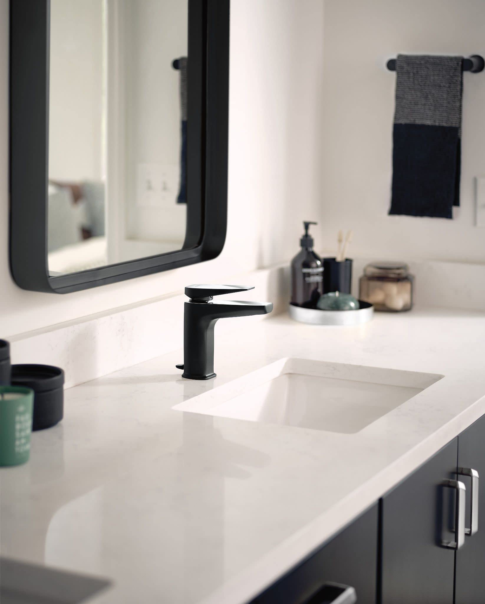 Black hand towel bar with cylindrical ends mounted on white bathroom wall above sink.
