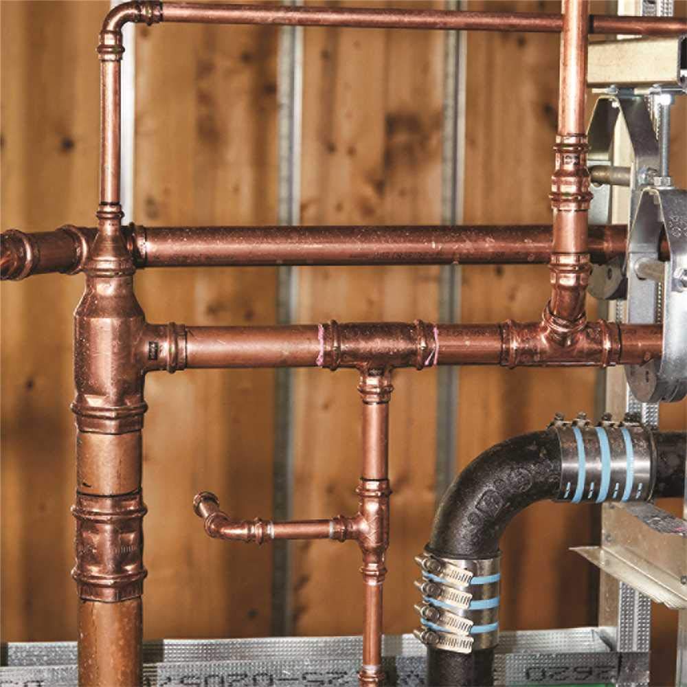 Copper press reducer fitting connecting two different-sized pipes in an assembled plumbing system.