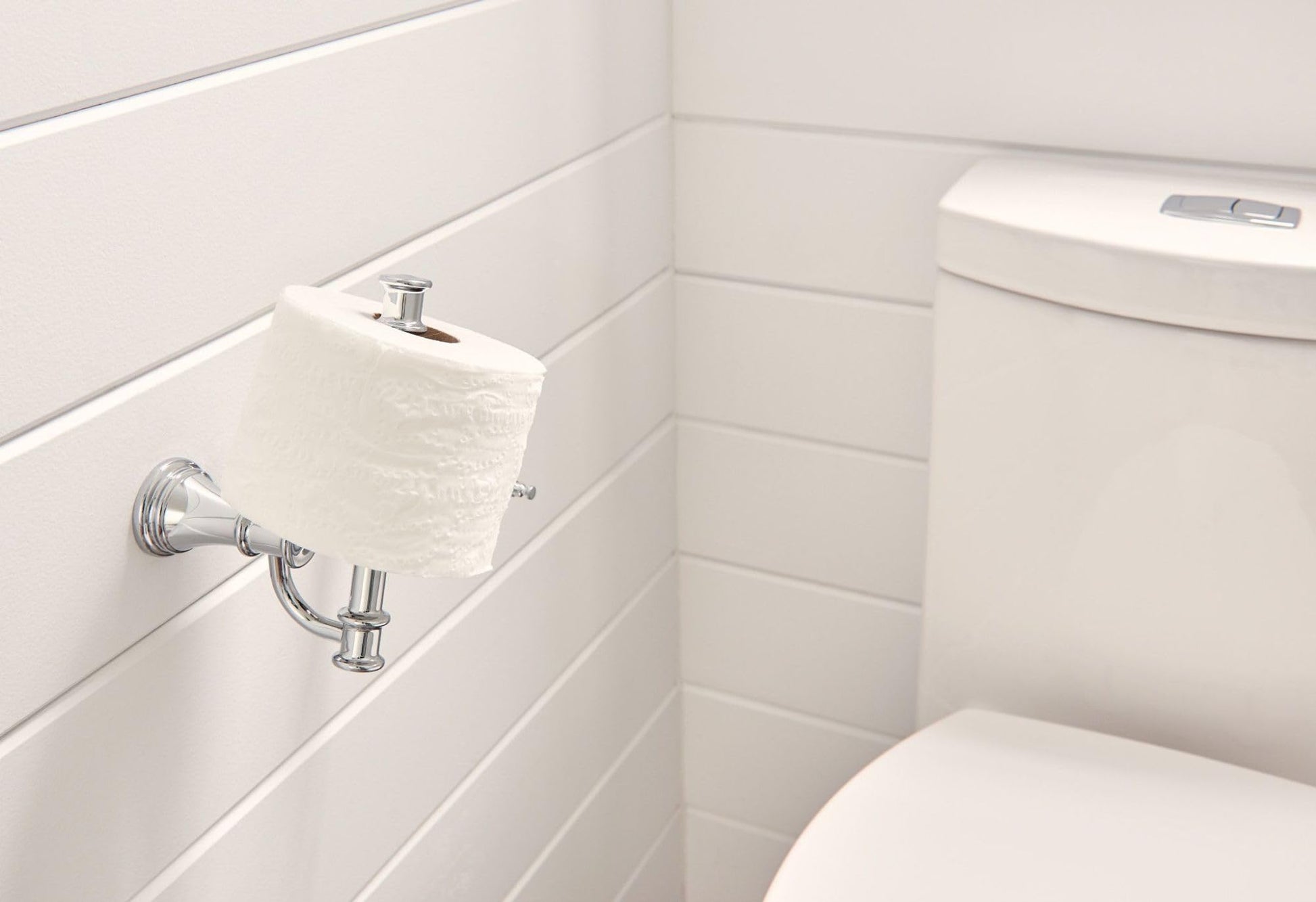 Chrome toilet paper holder mounted on white bathroom wall with roll of white tissue paper installed.