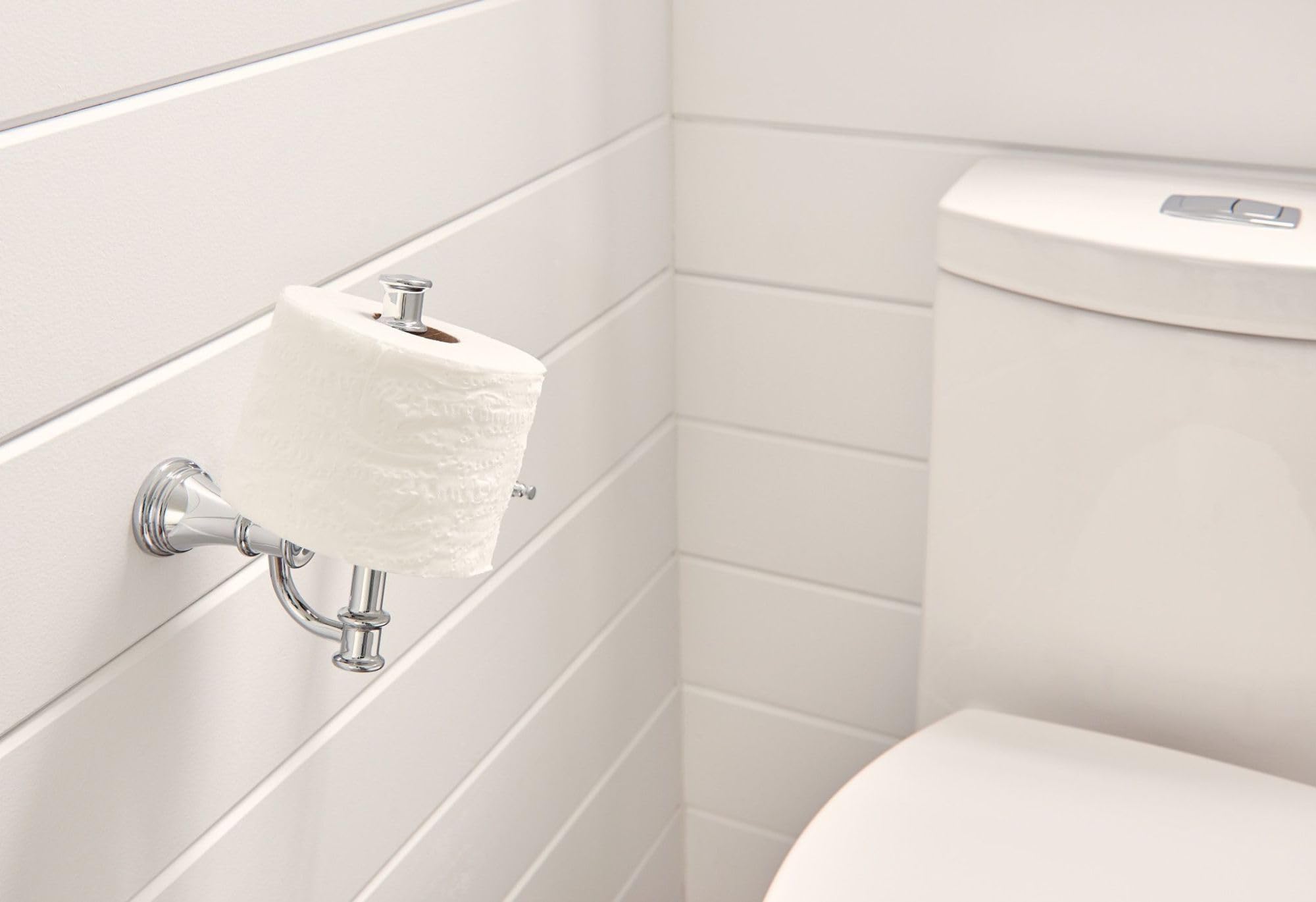 Chrome toilet paper holder mounted on white bathroom wall with roll of white tissue paper installed.