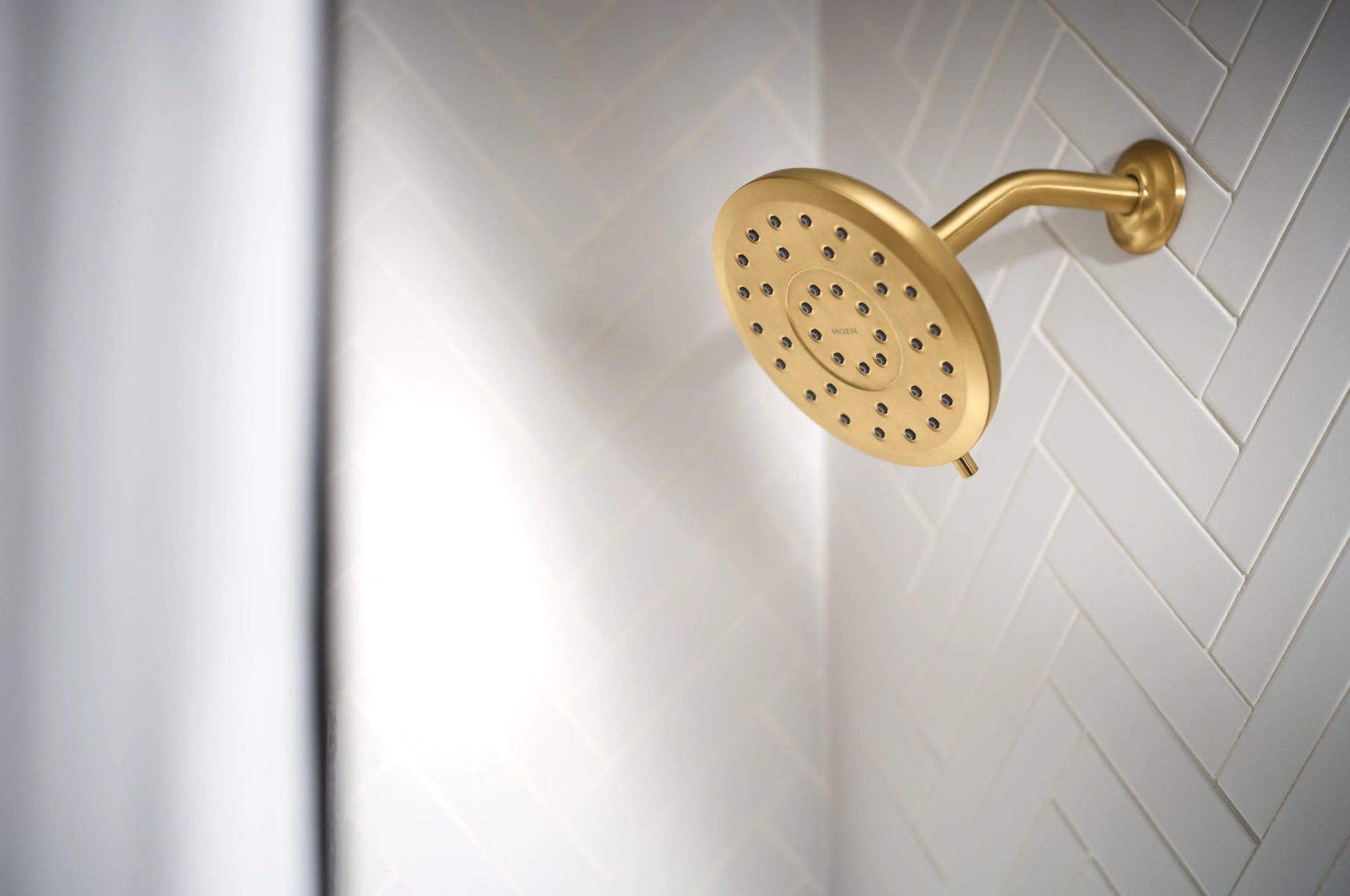 Brushed gold round rain showerhead with multiple spray holes mounted on angled wall bracket.