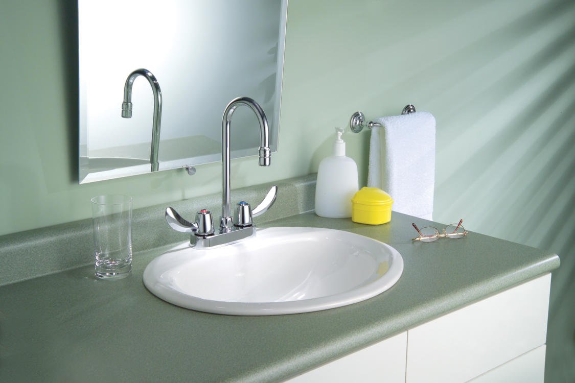 Chrome two-handle centerset bathroom faucet with gooseneck spout mounted above white round sink on green countertop.