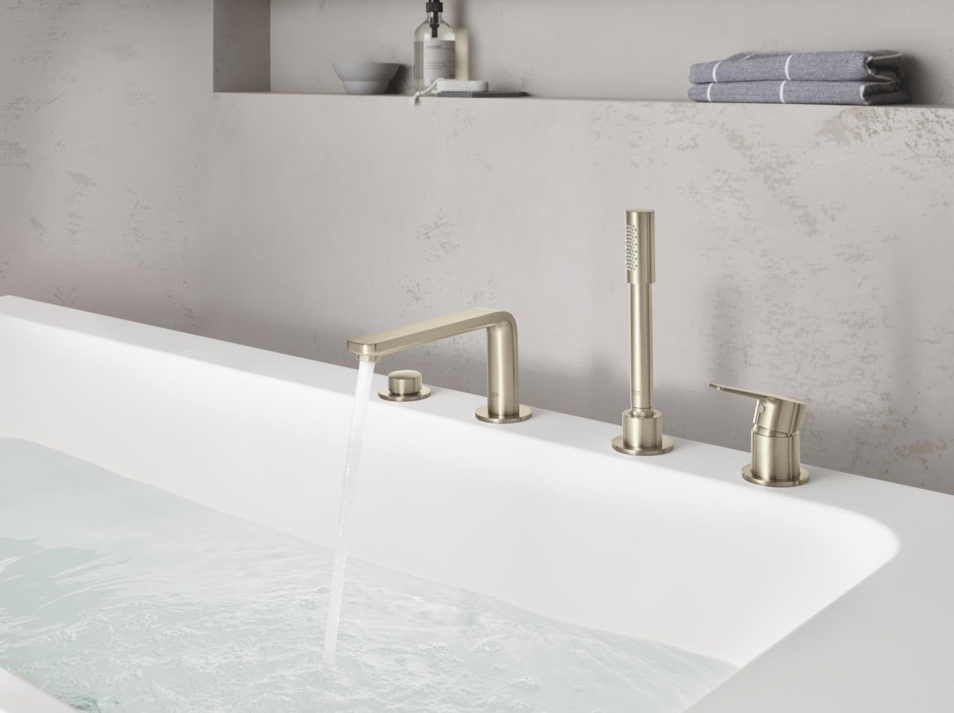 Brushed nickel four-piece deck-mount tub faucet with arched spout, vertical riser, and handheld shower head installed on whit