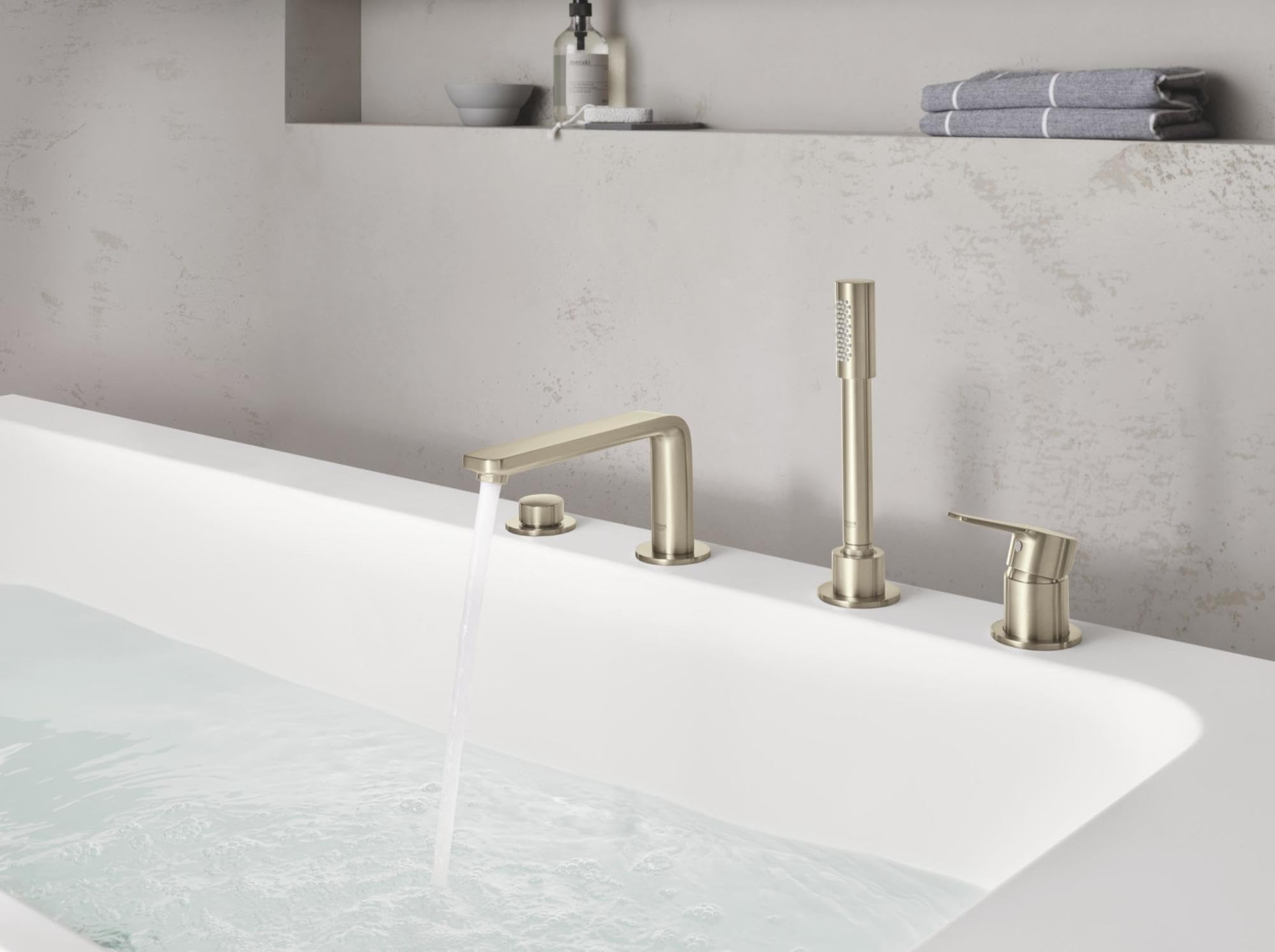 Brushed nickel four-piece deck-mount tub faucet with arched spout, vertical riser, and handheld shower head installed on whit