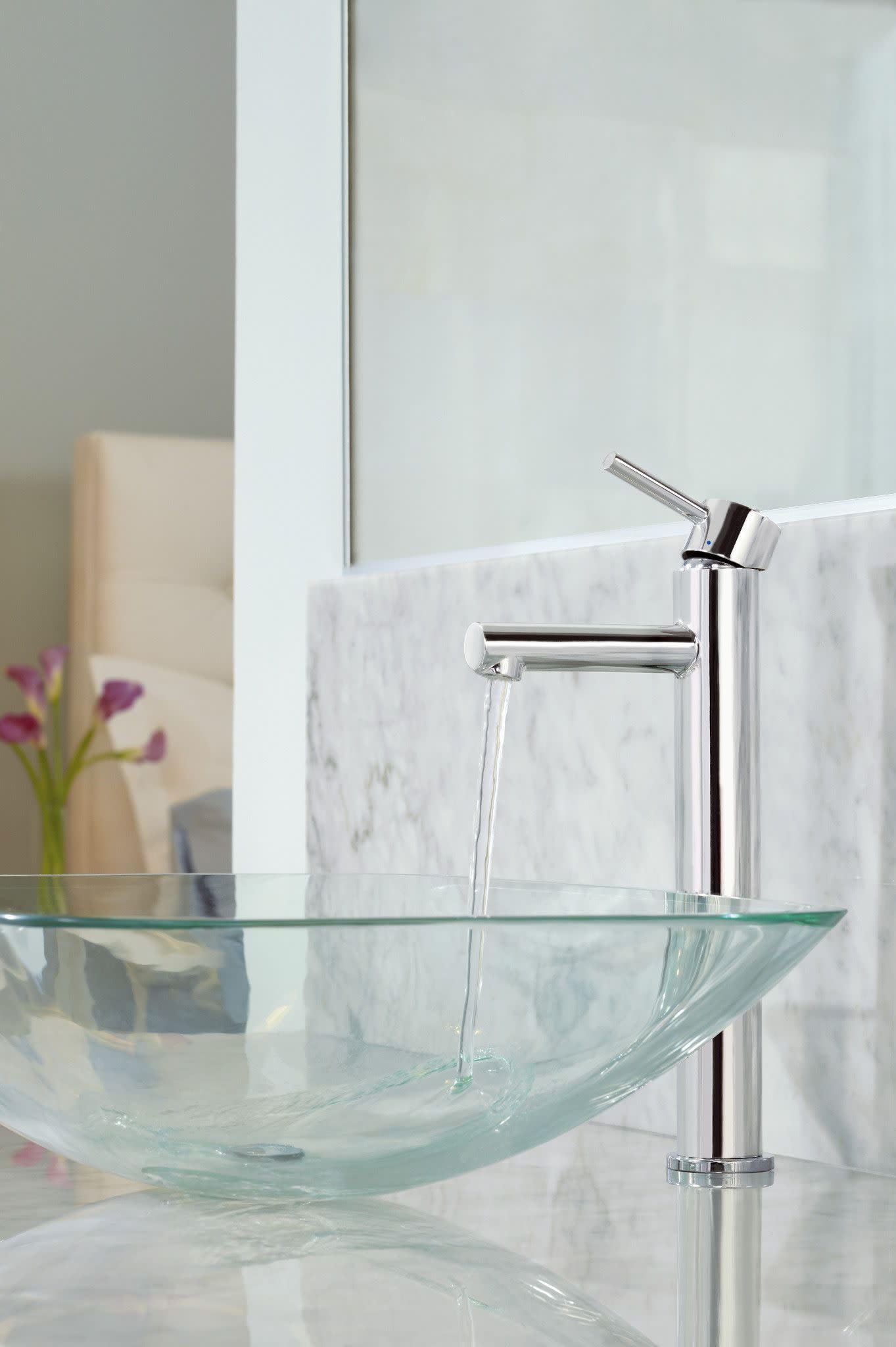 Brushed nickel single-handle faucet with tall spout mounted on glass vessel sink with marble backsplash.