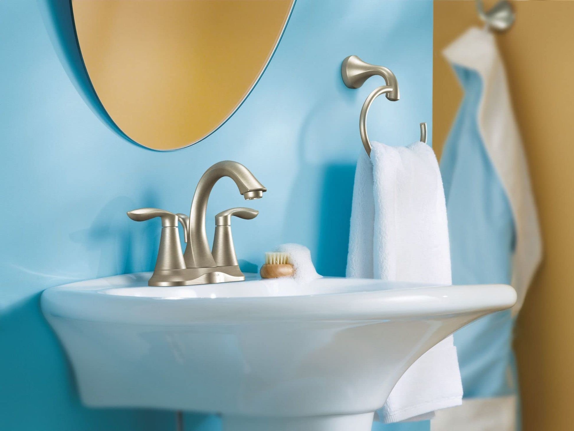 Brushed nickel wall-mount robe hook with curved design holding white towel in bathroom.
