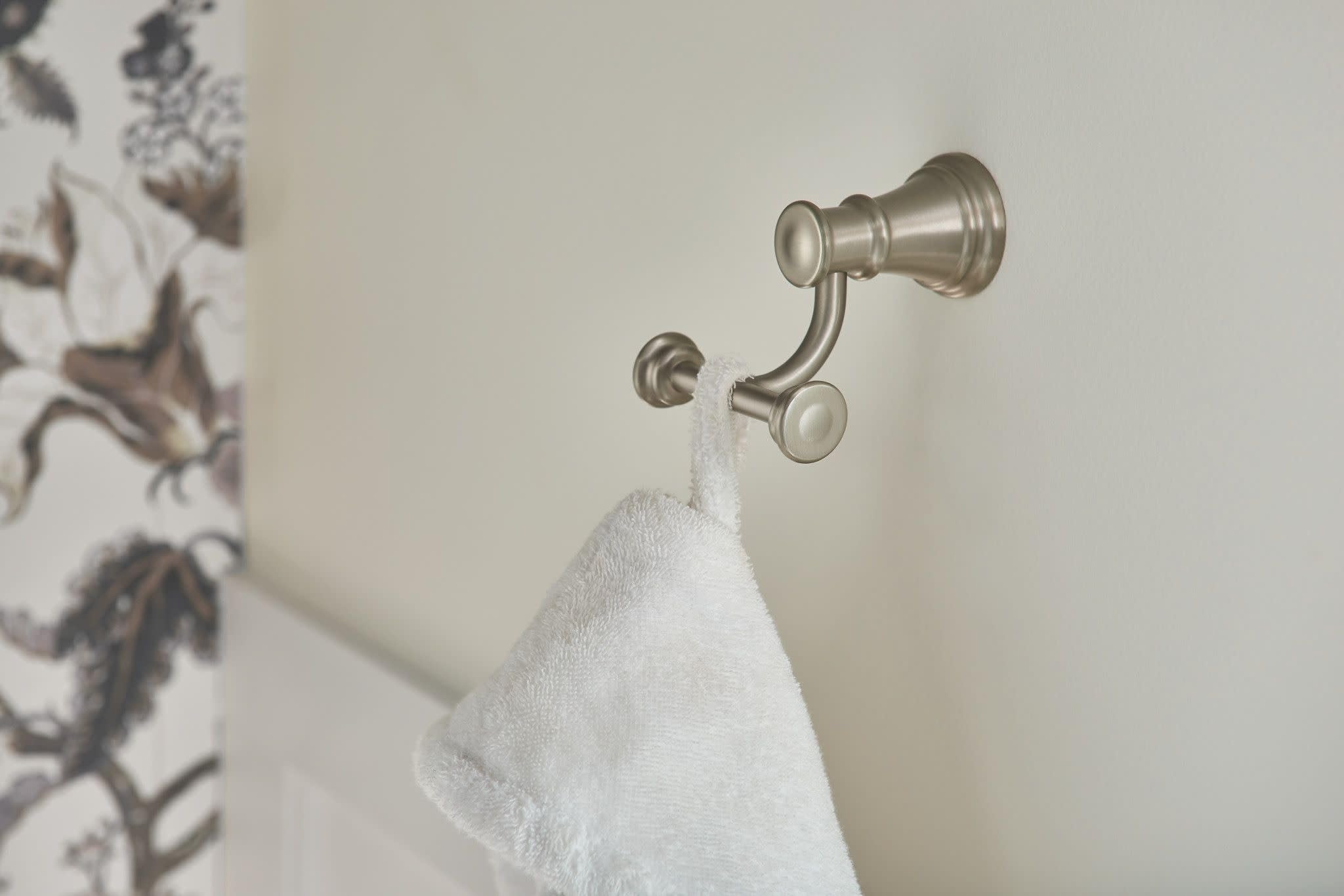 Brushed nickel double robe hook mounted on wall with white towel draped over hooks.