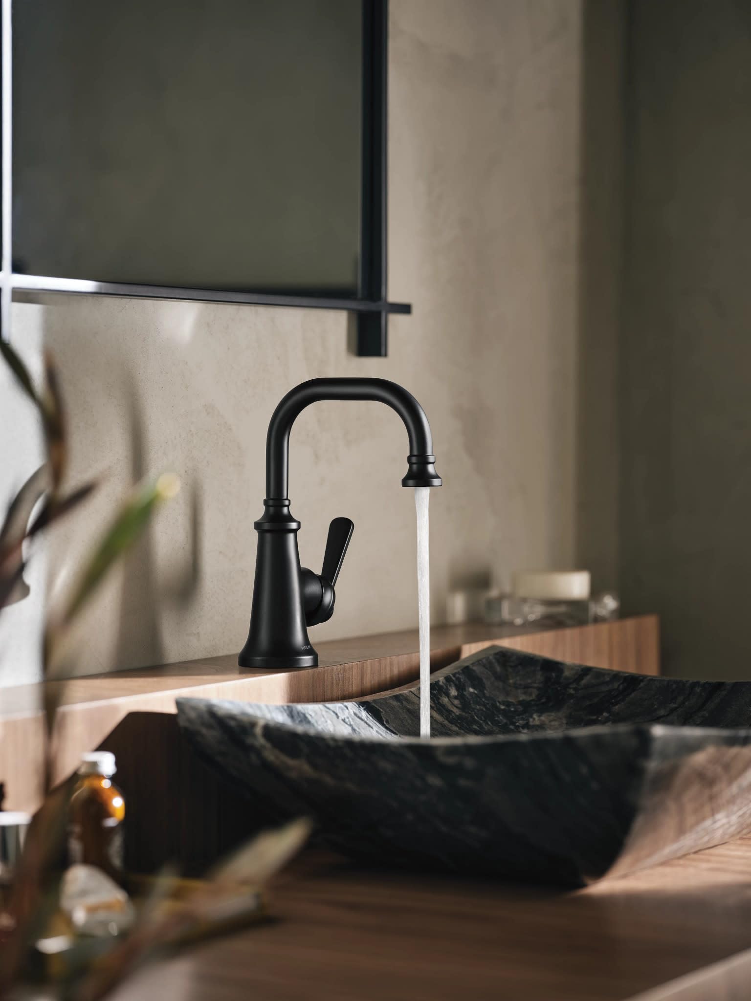 Matte black single-handle bathroom faucet with curved spout and lever handle mounted above a dark stone vessel sink.