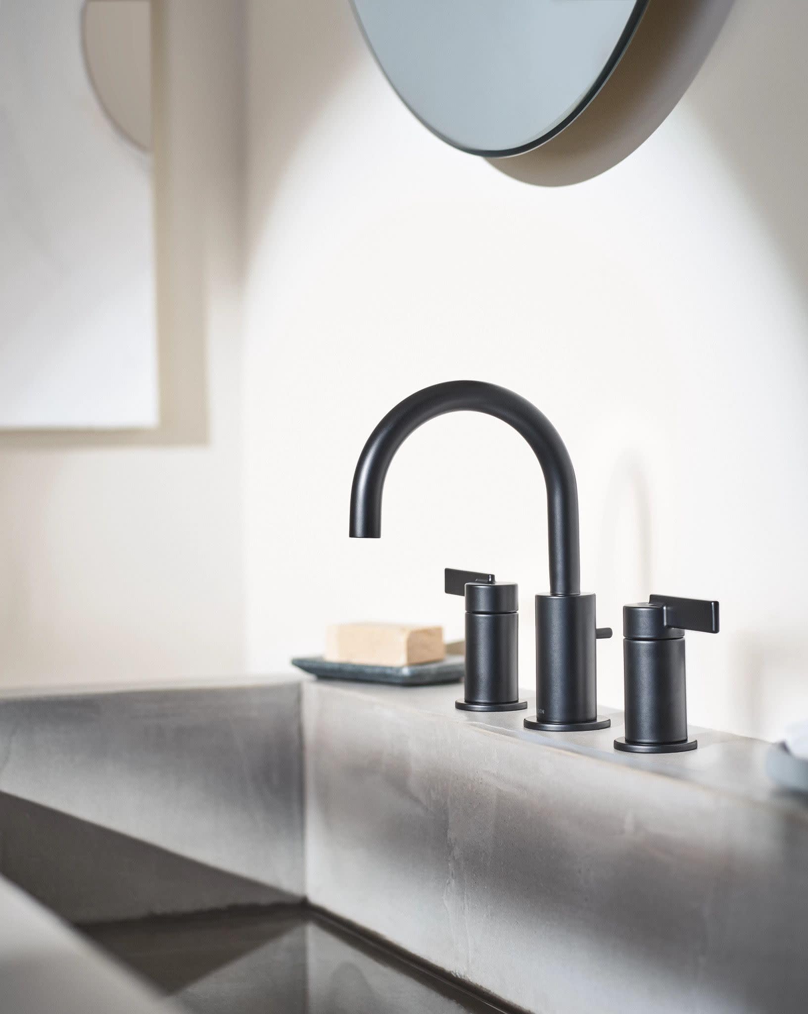 Matte black two-handle high-arc bathroom faucet with lever handles installed on white sink.