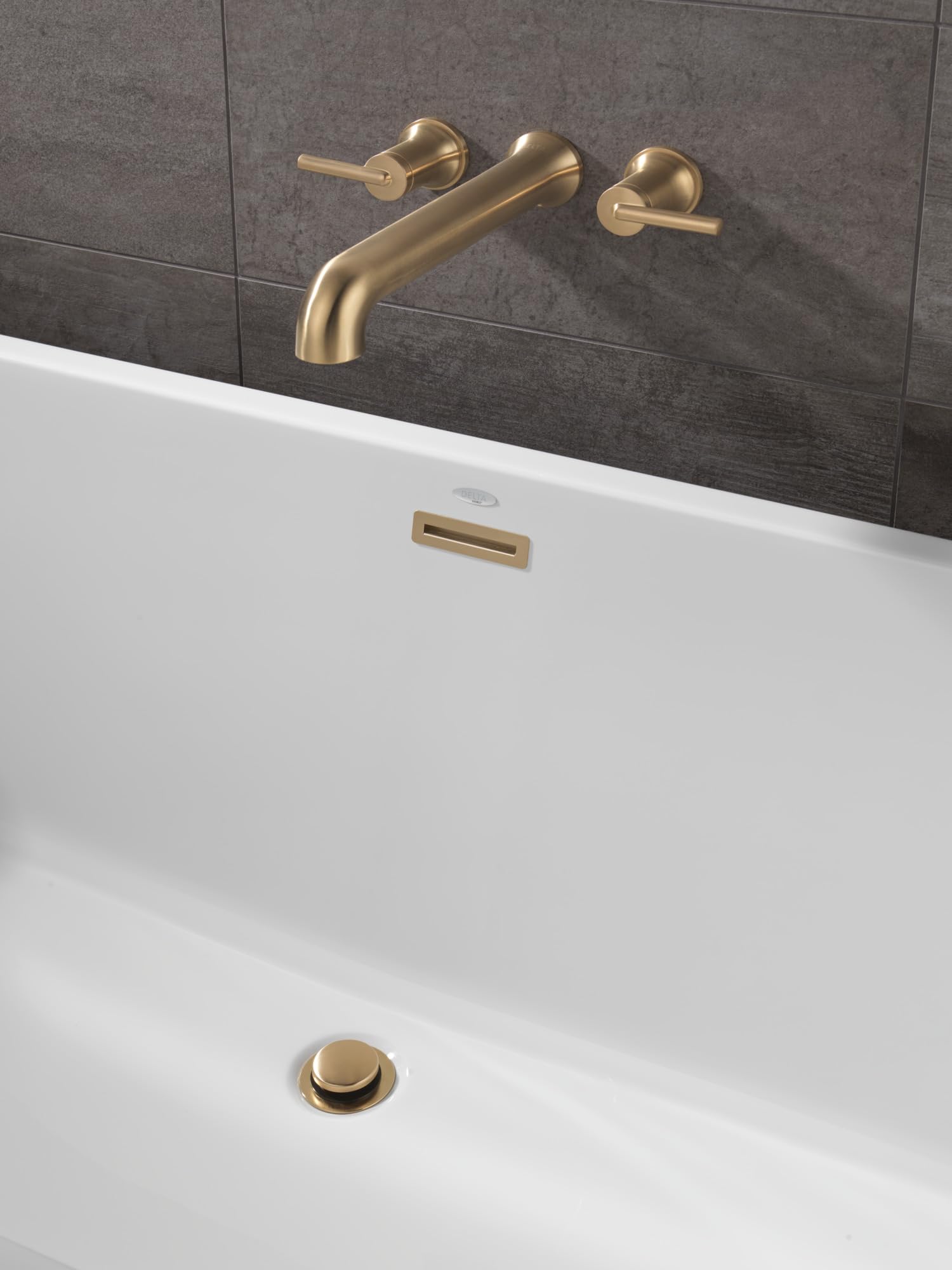 Champagne bronze wall-mounted tub faucet with curved spout and lever handles, showing drain and overflow openings on white tu