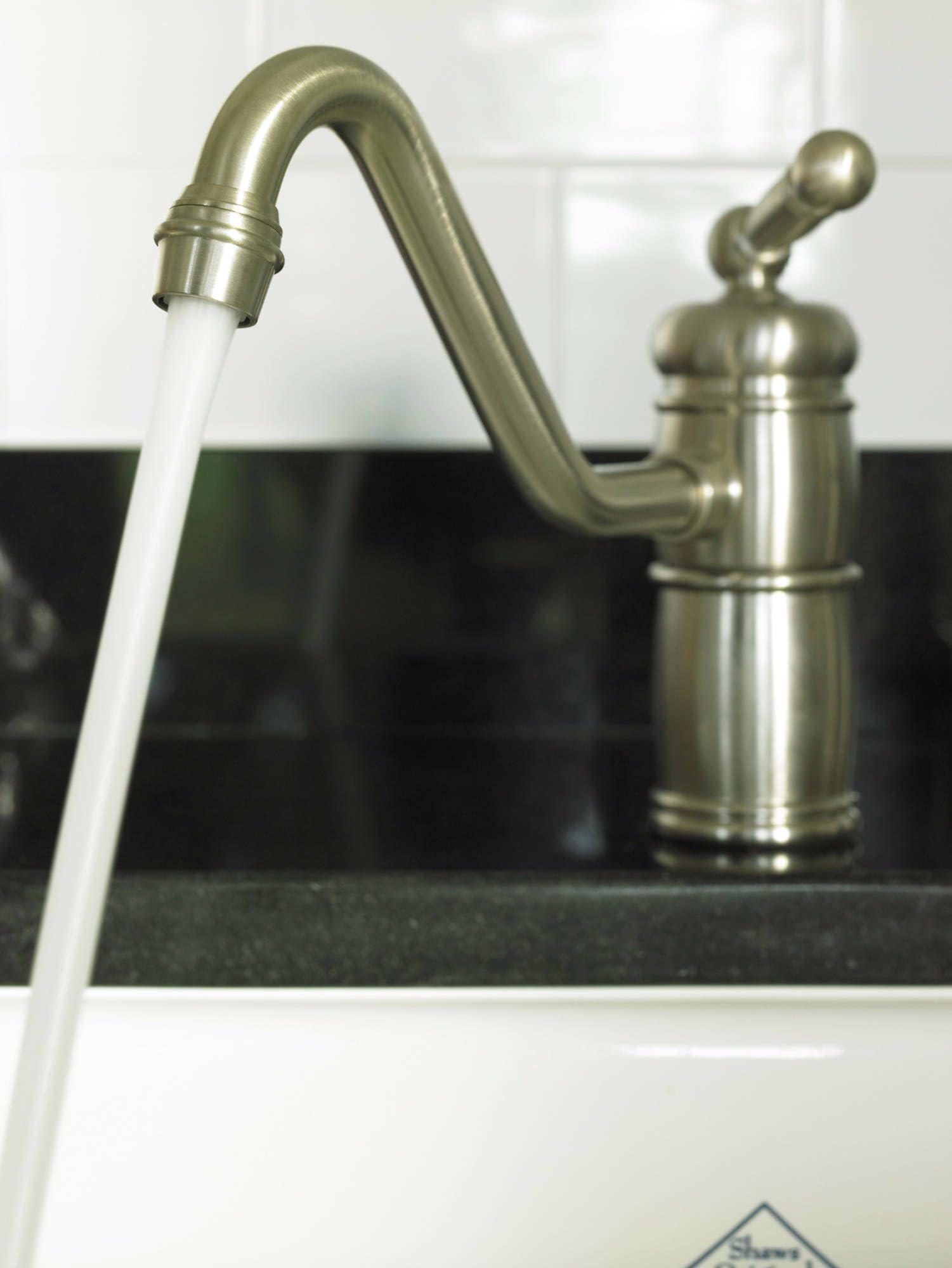 Satin nickel single-handle kitchen faucet with curved spout and ball handle, water running from aerator.