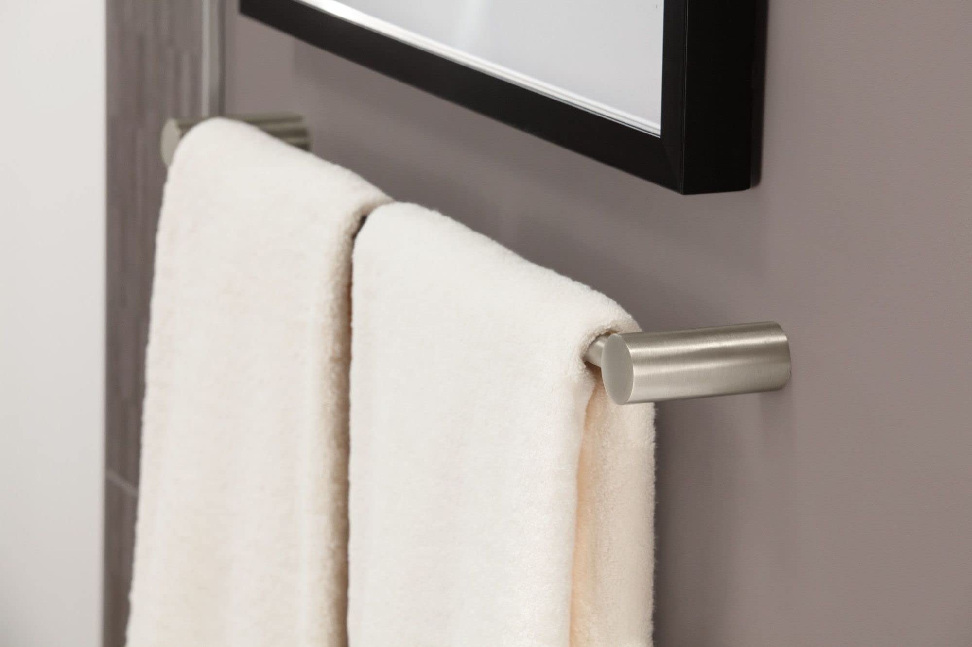 Brushed nickel wall-mounted towel bar with two folded white towels draped over it against a gray wall.