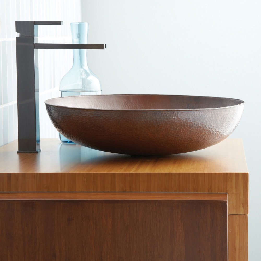 Antique copper vessel sink with hammered finish and matte black single-lever faucet on wooden vanity.