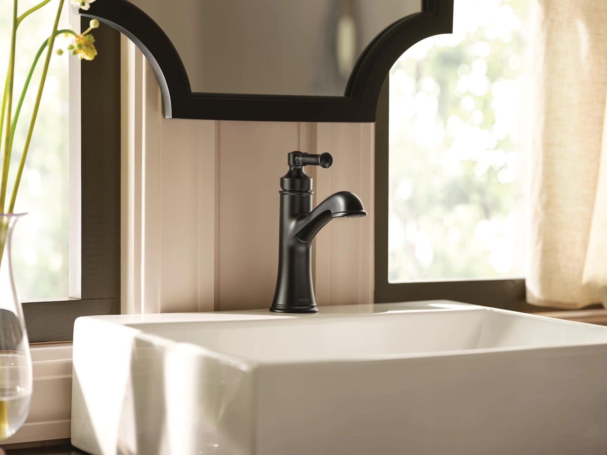Matte black single-handle bathroom sink faucet with curved spout installed on white vessel sink.