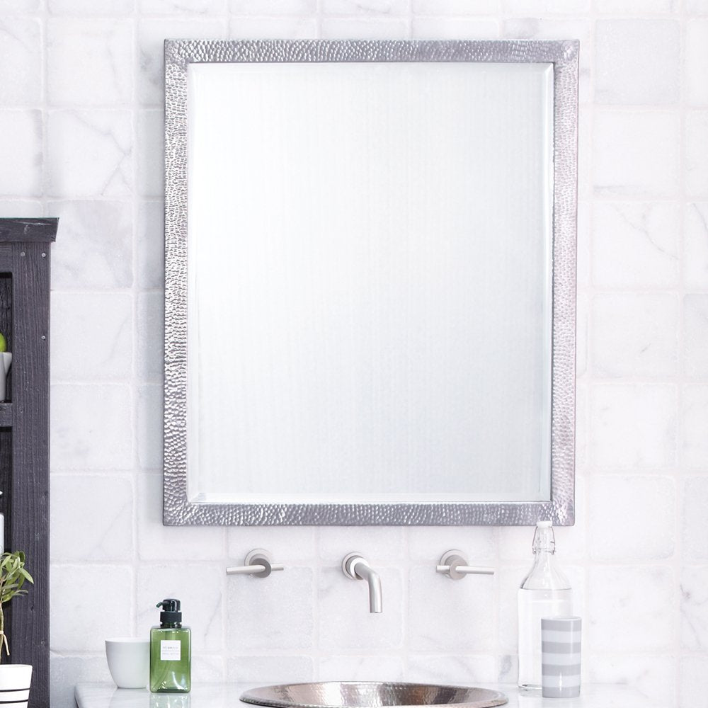 Rectangular mirror with textured silver frame mounted above bathroom sink with marble tile wall.