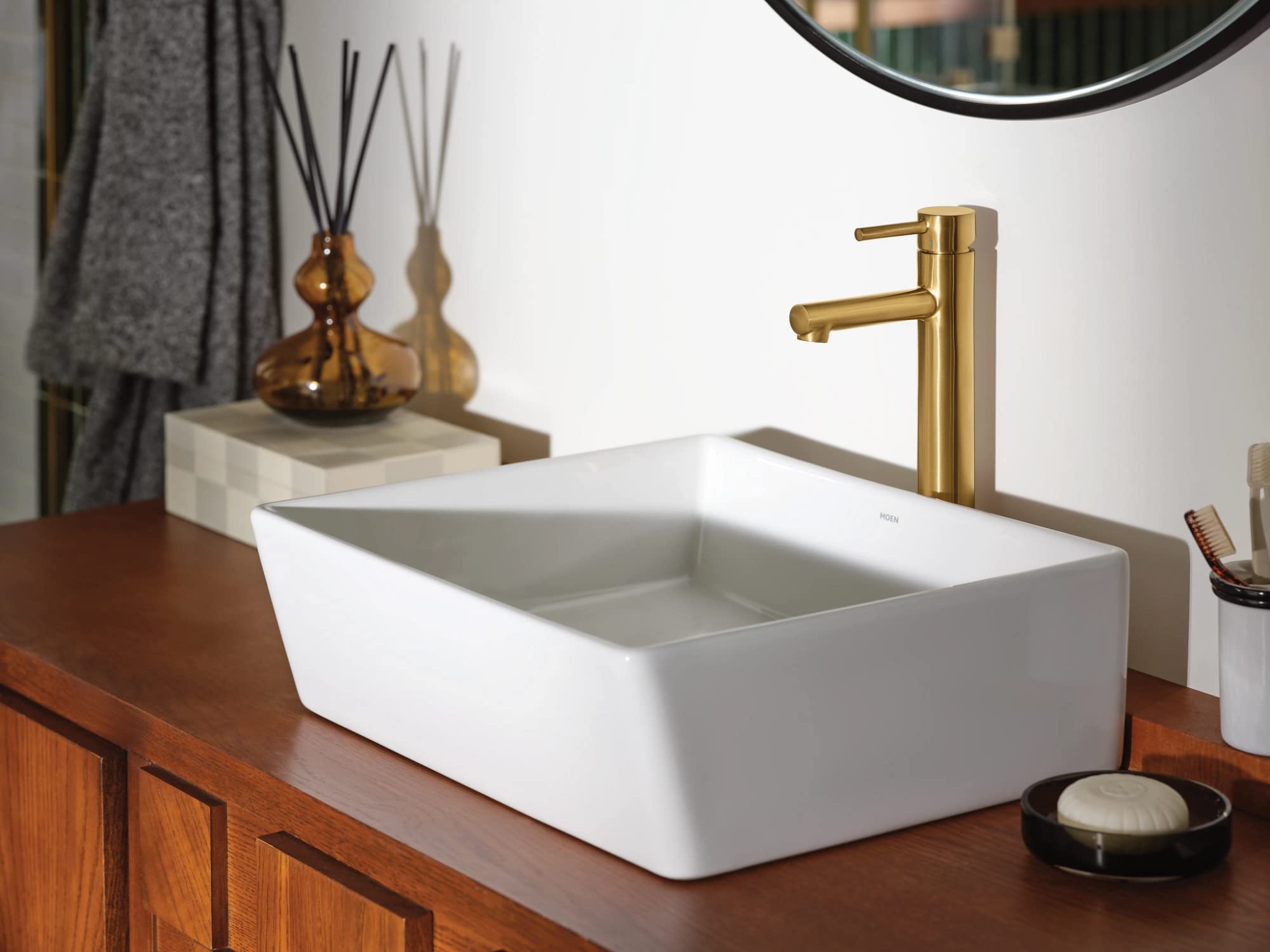 Brushed gold single-handle faucet with cylindrical spout mounted on white rectangular vessel sink.