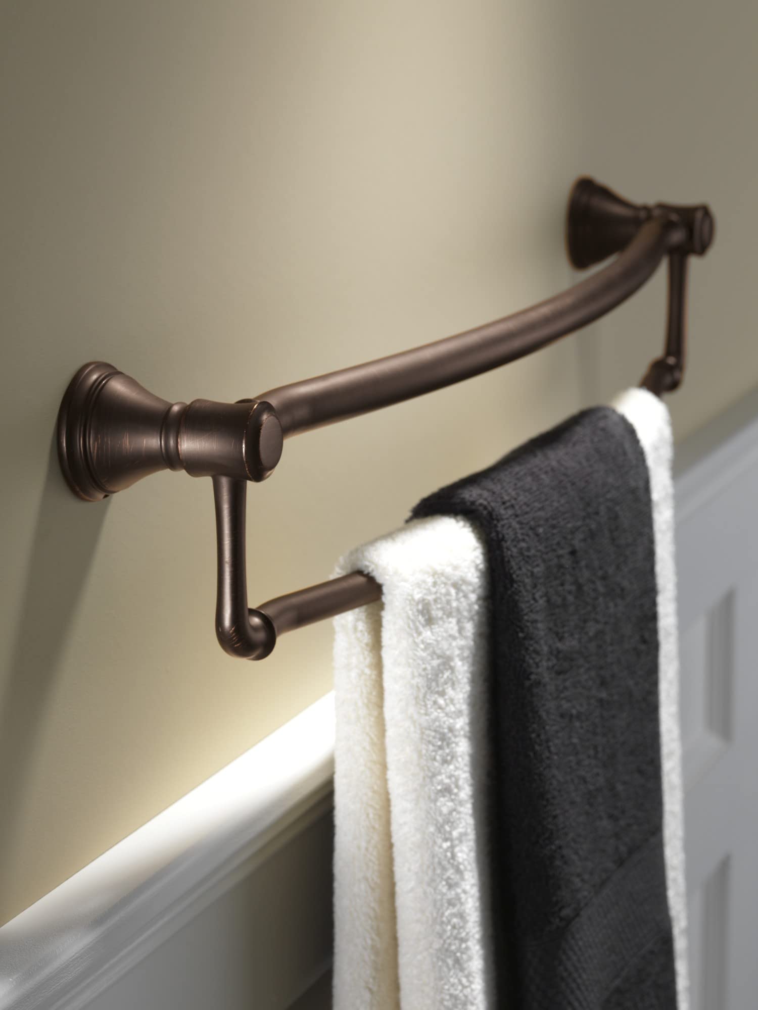 Stainless steel towel bar with assist grip in oil-rubbed bronze finish mounted on wall with towels draped over bar.