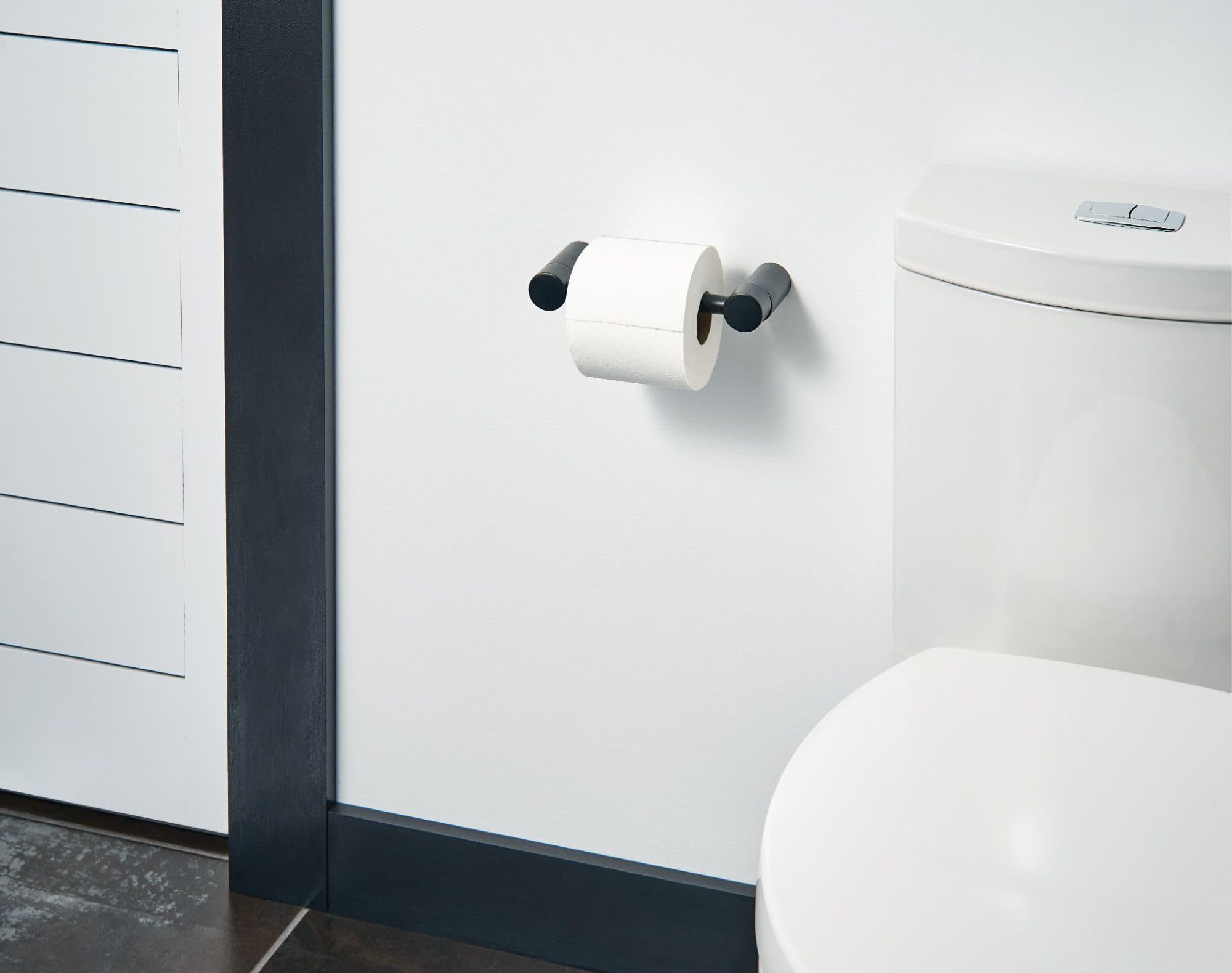 Black and chrome pivoting toilet paper holder mounted on white bathroom wall with white roll installed.