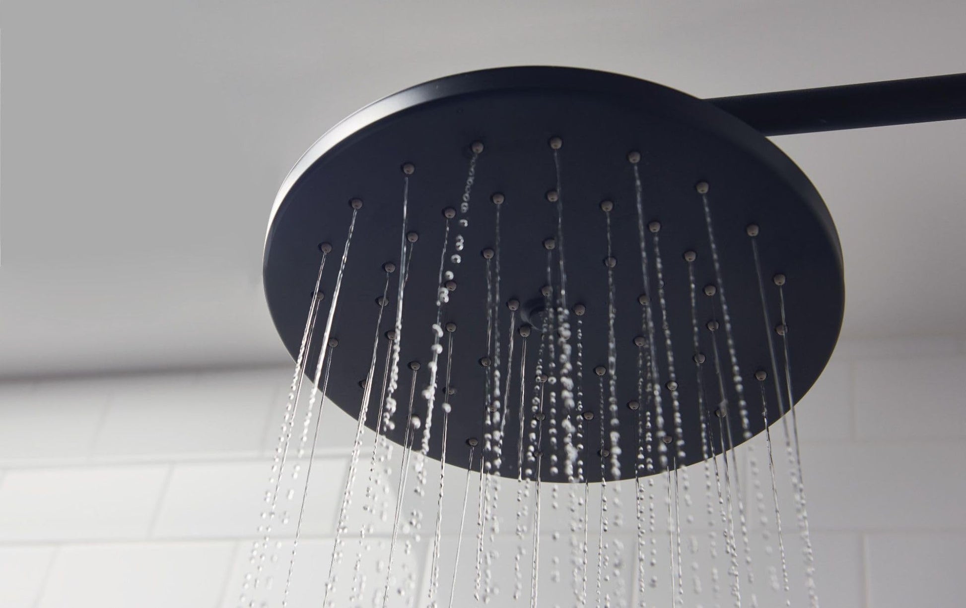 Dark wrought iron round showerhead with multiple water jets and curved arm against white background.