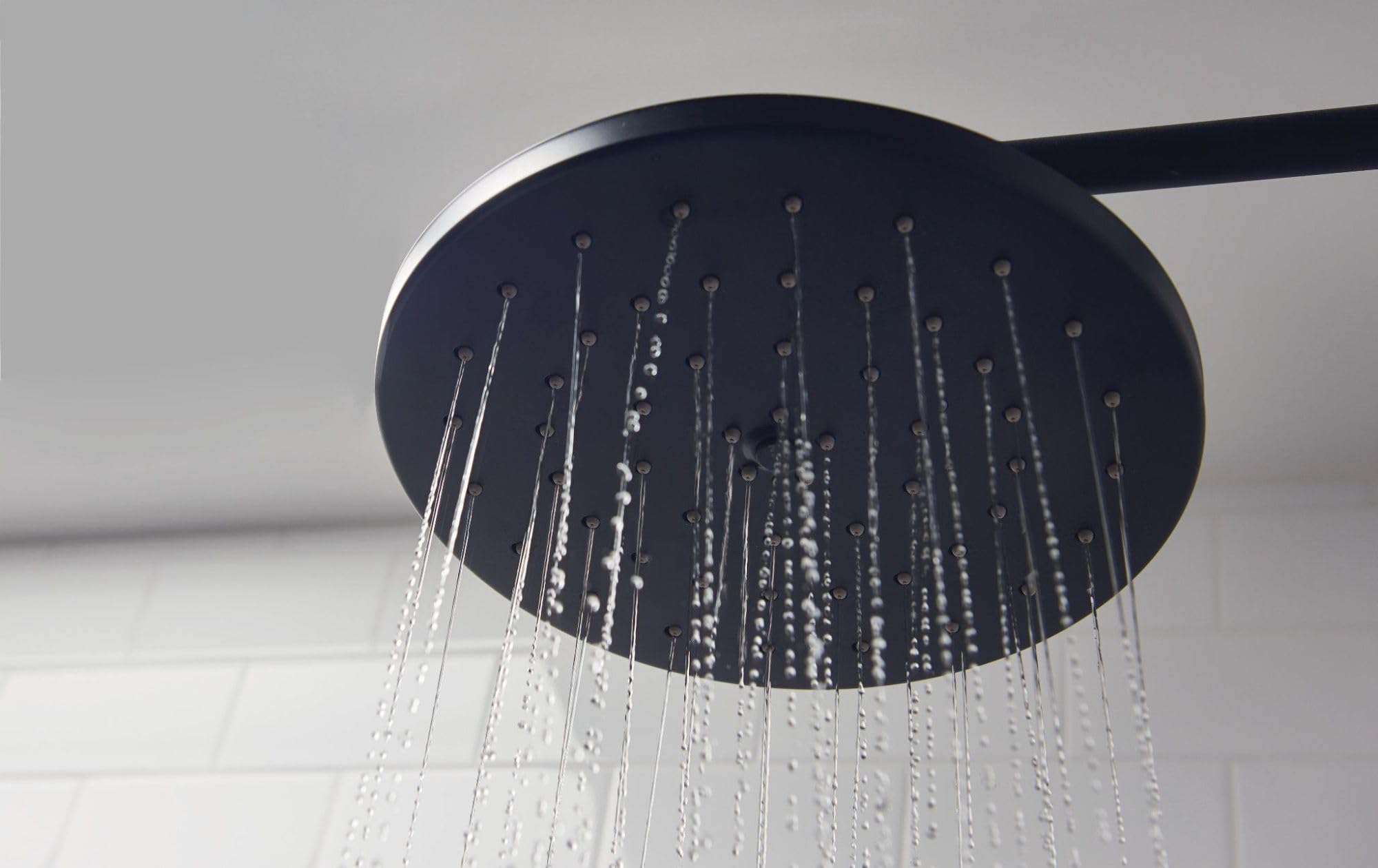 Dark wrought iron round showerhead with multiple water jets and curved arm against white background.