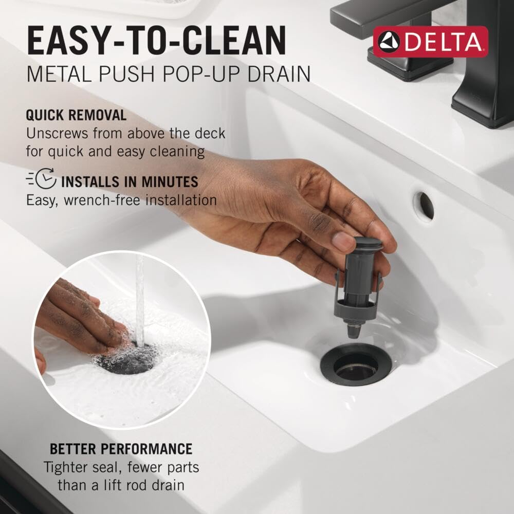 Matte black metal push pop-up drain installed in white sink with hand demonstrating removal mechanism.