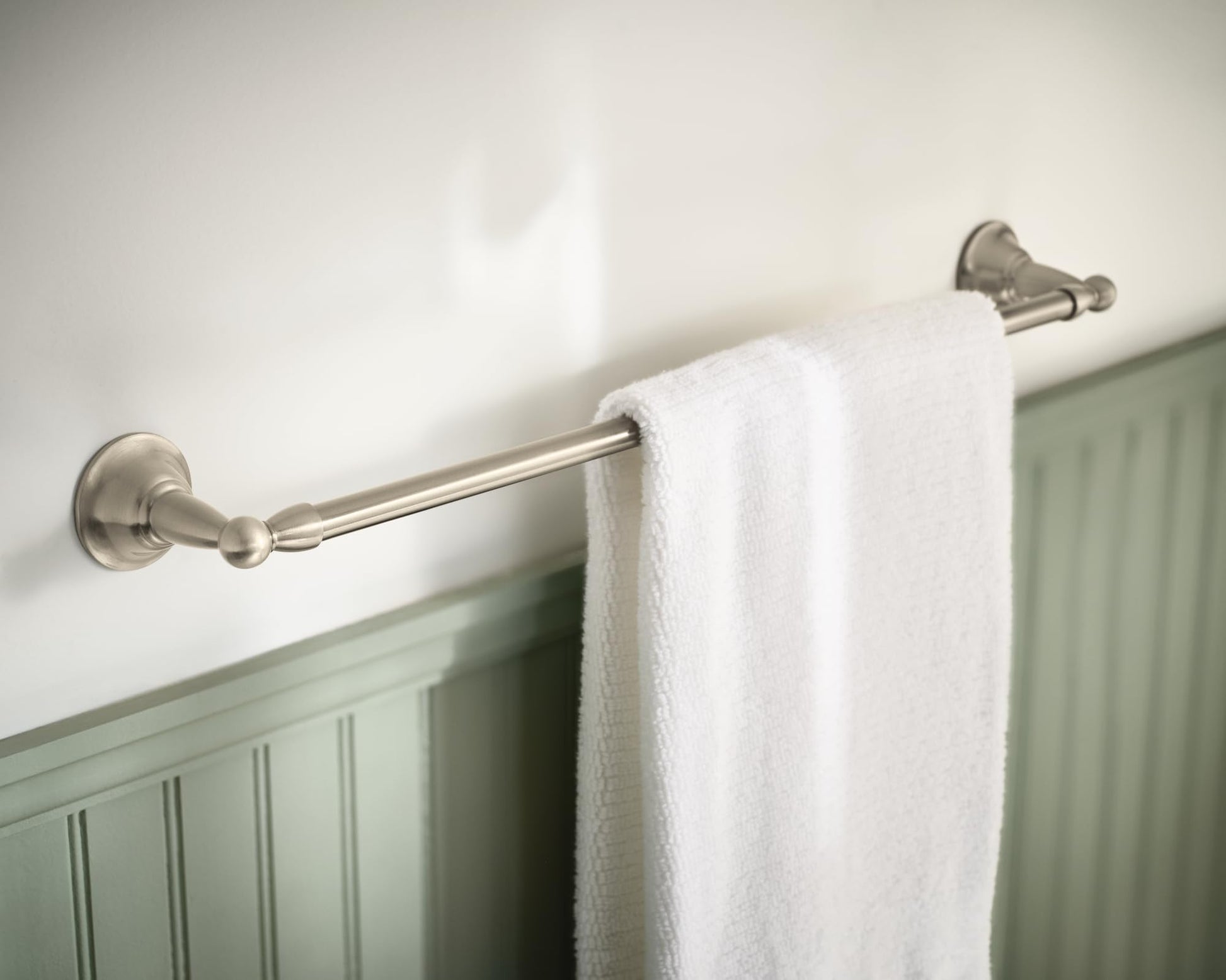 Brushed nickel towel bar mounted on wall with white towel draped over it.