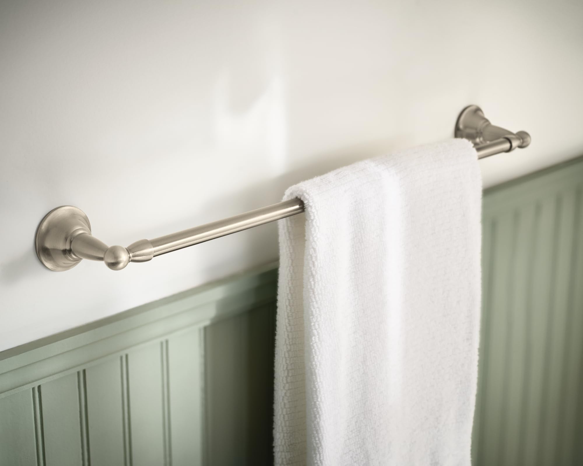 Brushed nickel towel bar mounted on wall with white towel draped over it.