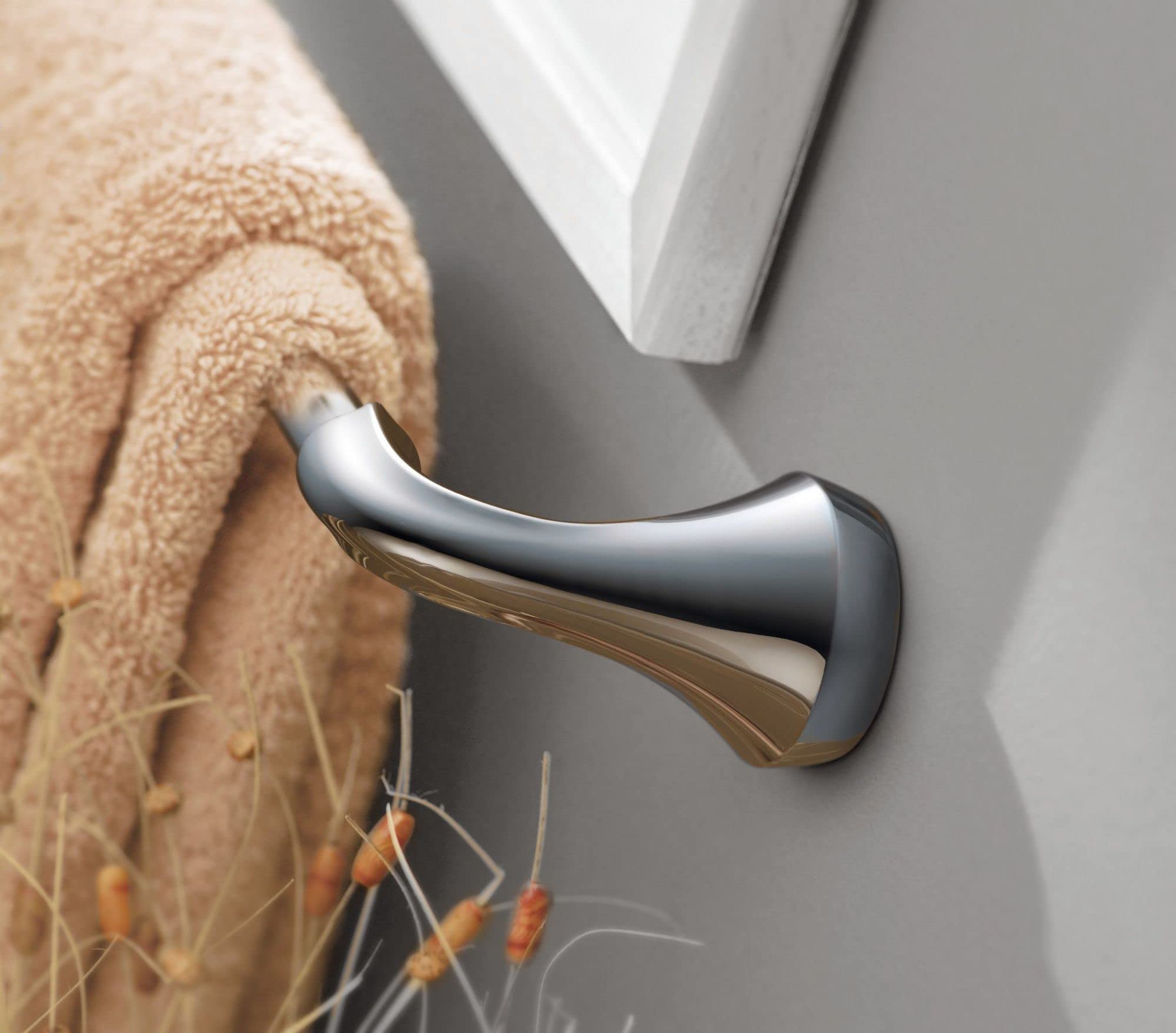 Polished chrome curved towel bar mounted on gray wall with beige towel draped over it.