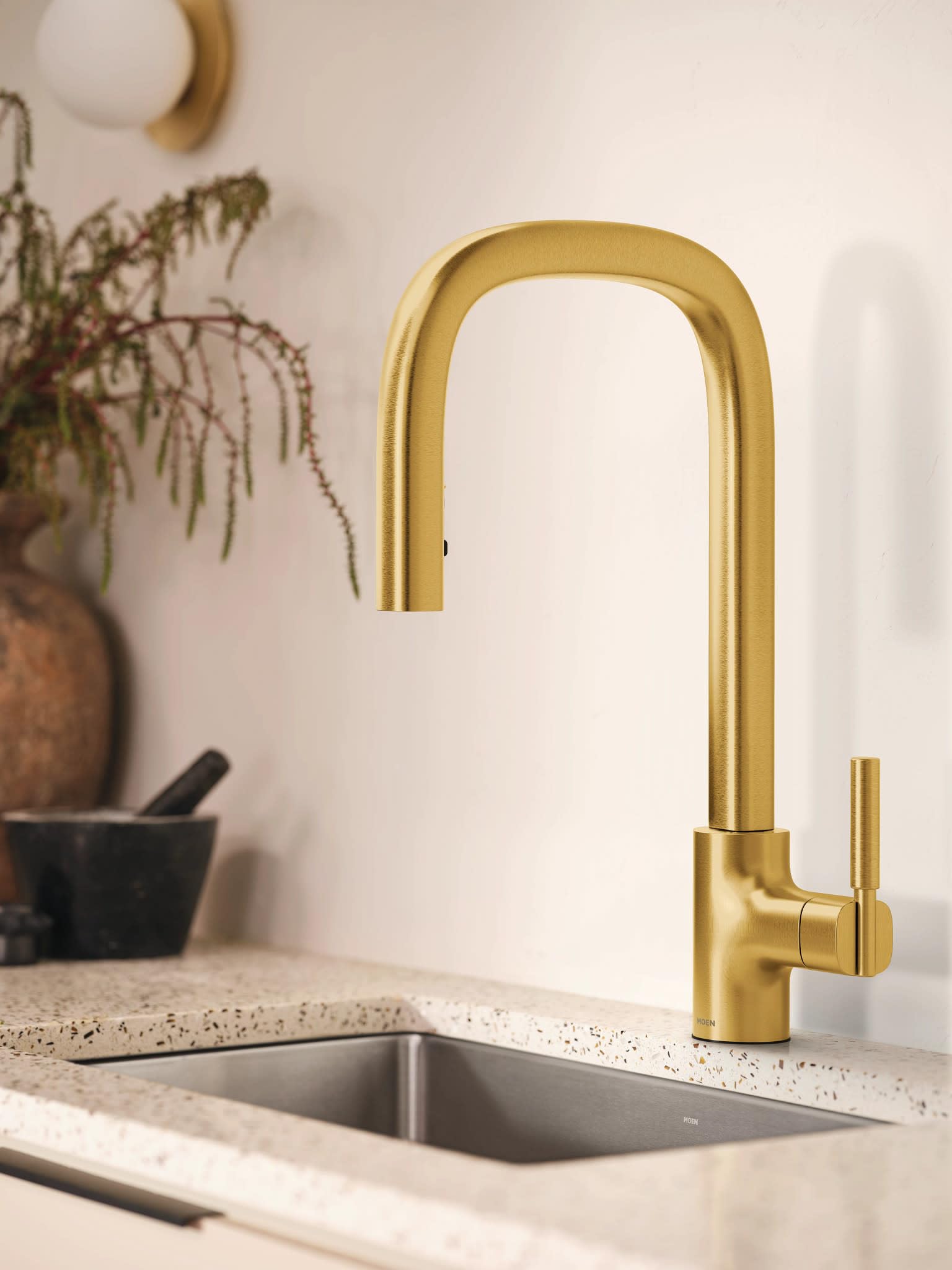 Brushed gold kitchen faucet with tall curved spout and single side handle mounted above stainless steel sink.