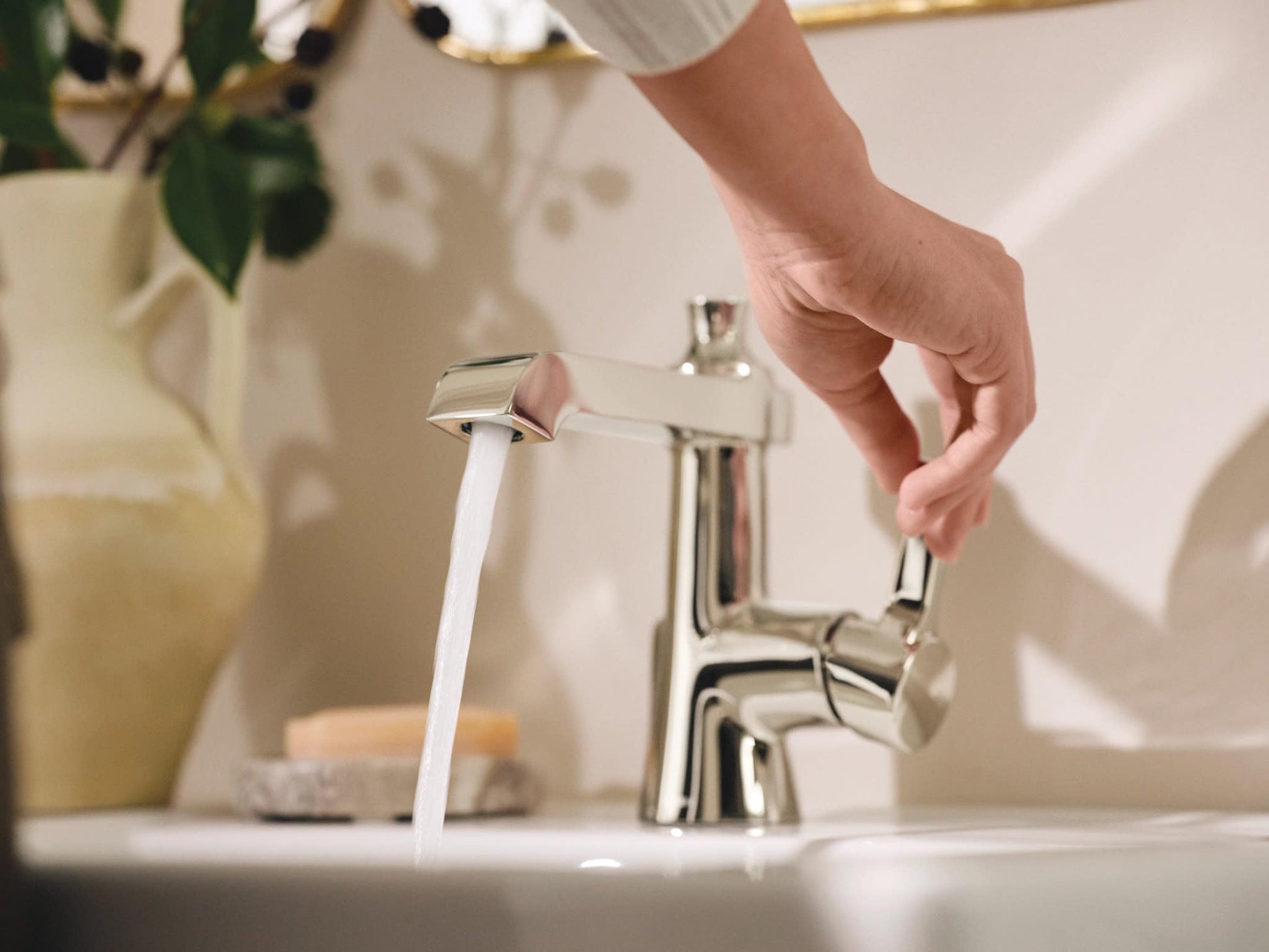 Polished nickel single-handle bathroom sink faucet with water running from spout over white sink.